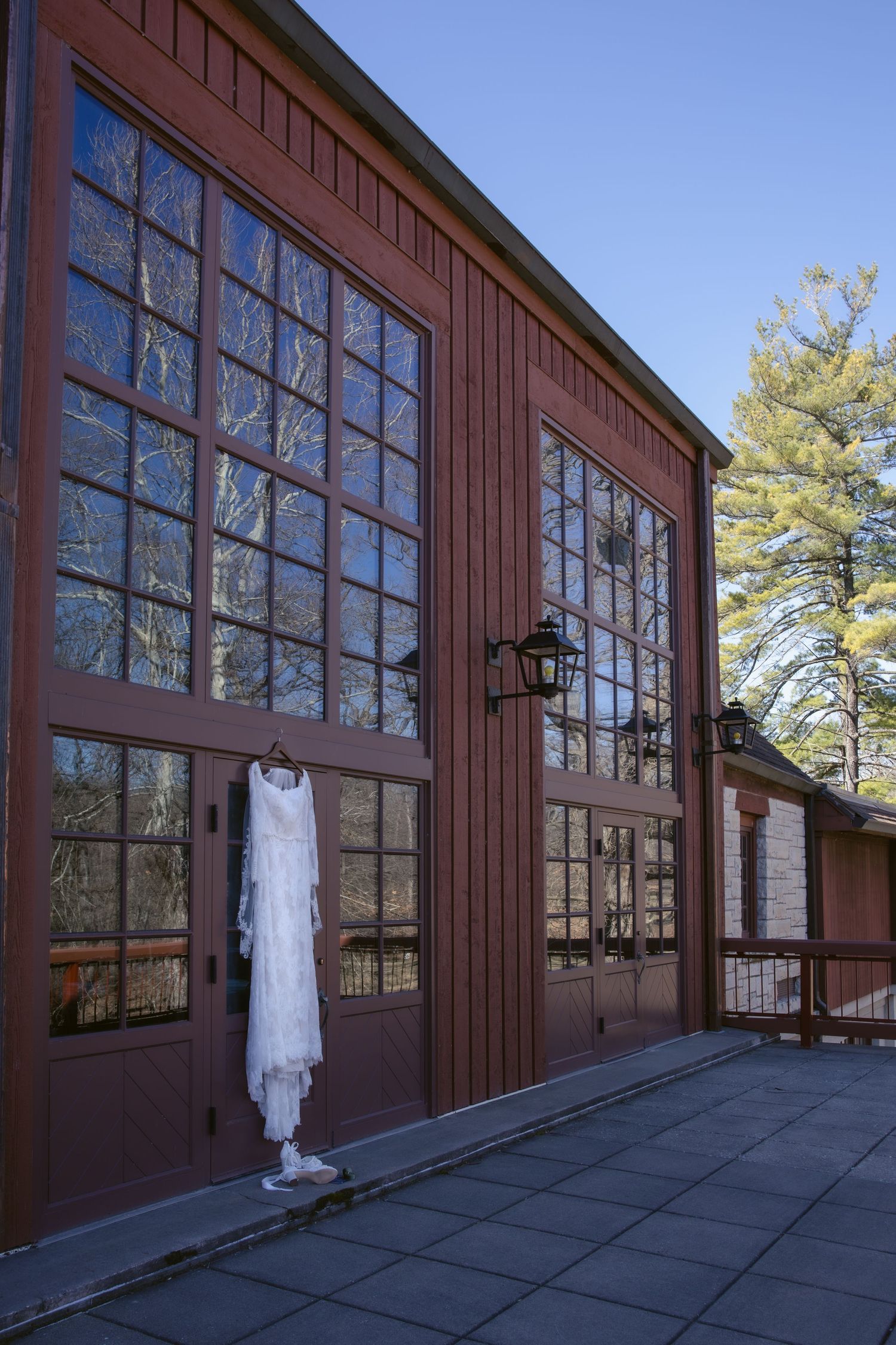 A long white dress hangs outside a rustic brown building with large windows and a lantern mounted on the wall.