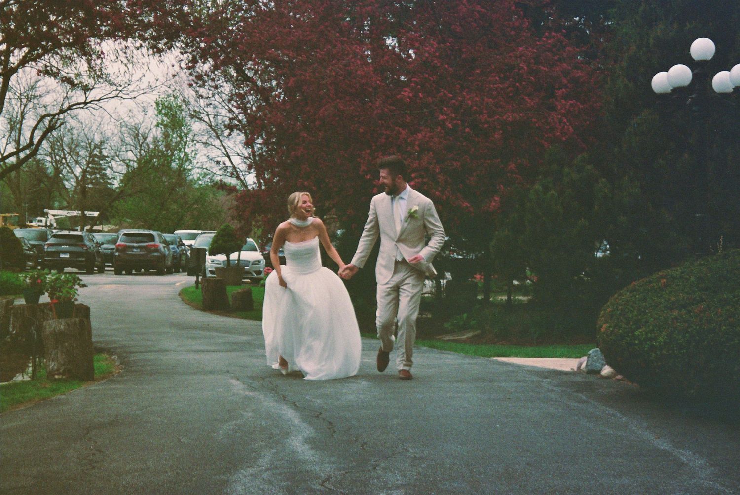 Bride and groom walking hand in hand on a tree-lined path during their outdoor wedding celebration.