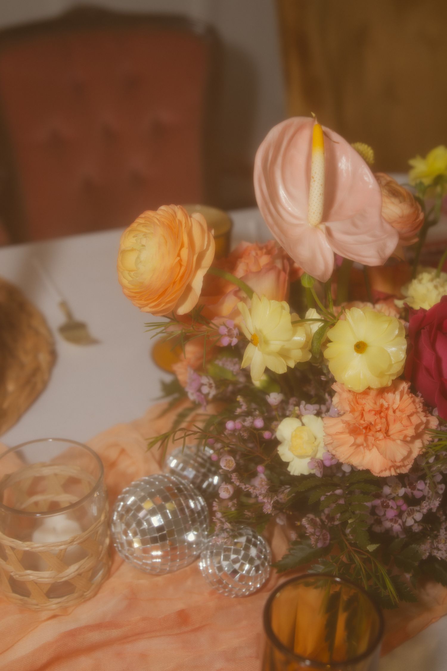 A romantic table setting with peach ranunculus, yellow flowers and disco ball decorations in warm ambient lighting.
