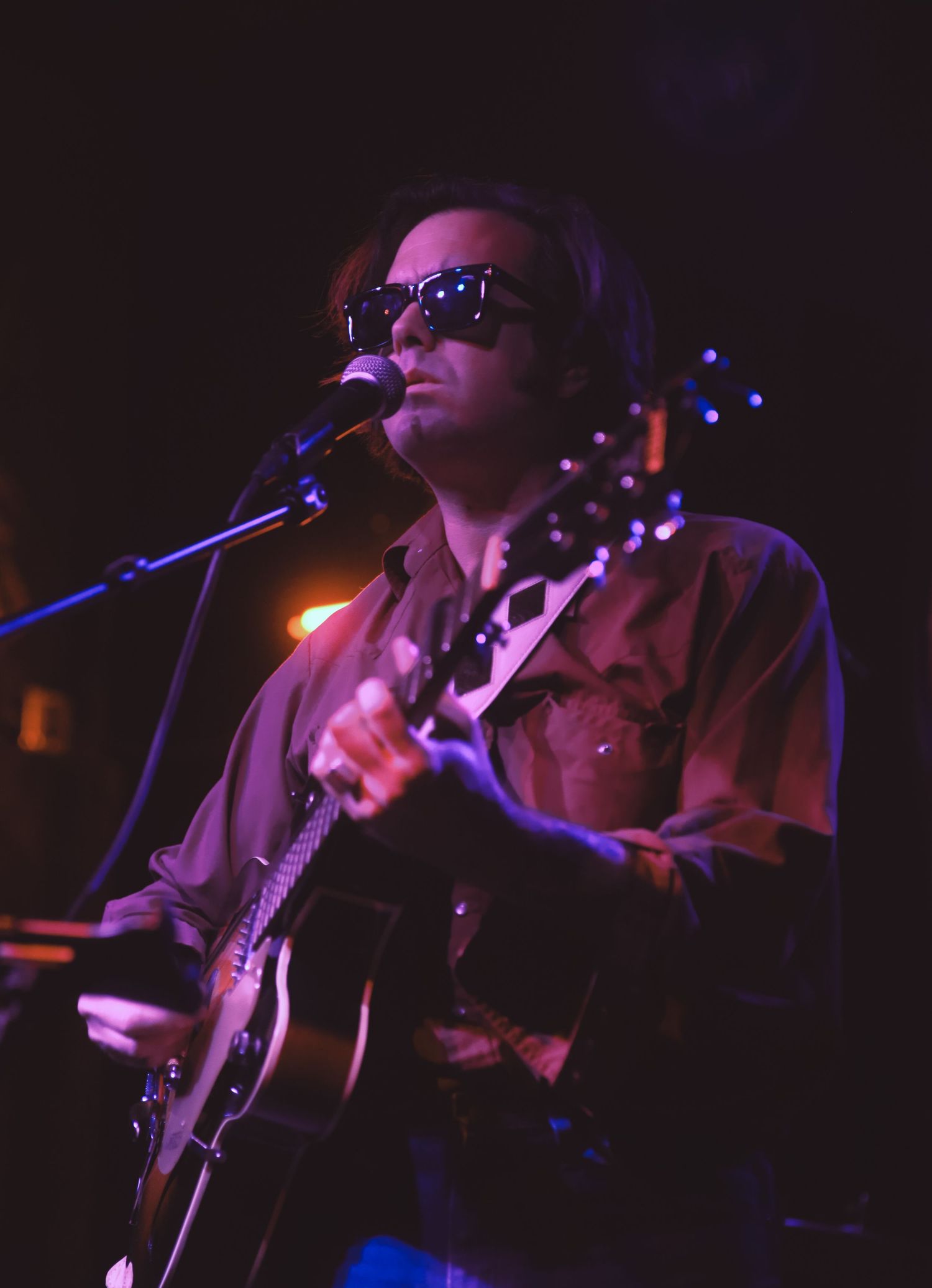 Musicians perform on stage in low lighting conditions with guitars and microphones during a live concert.