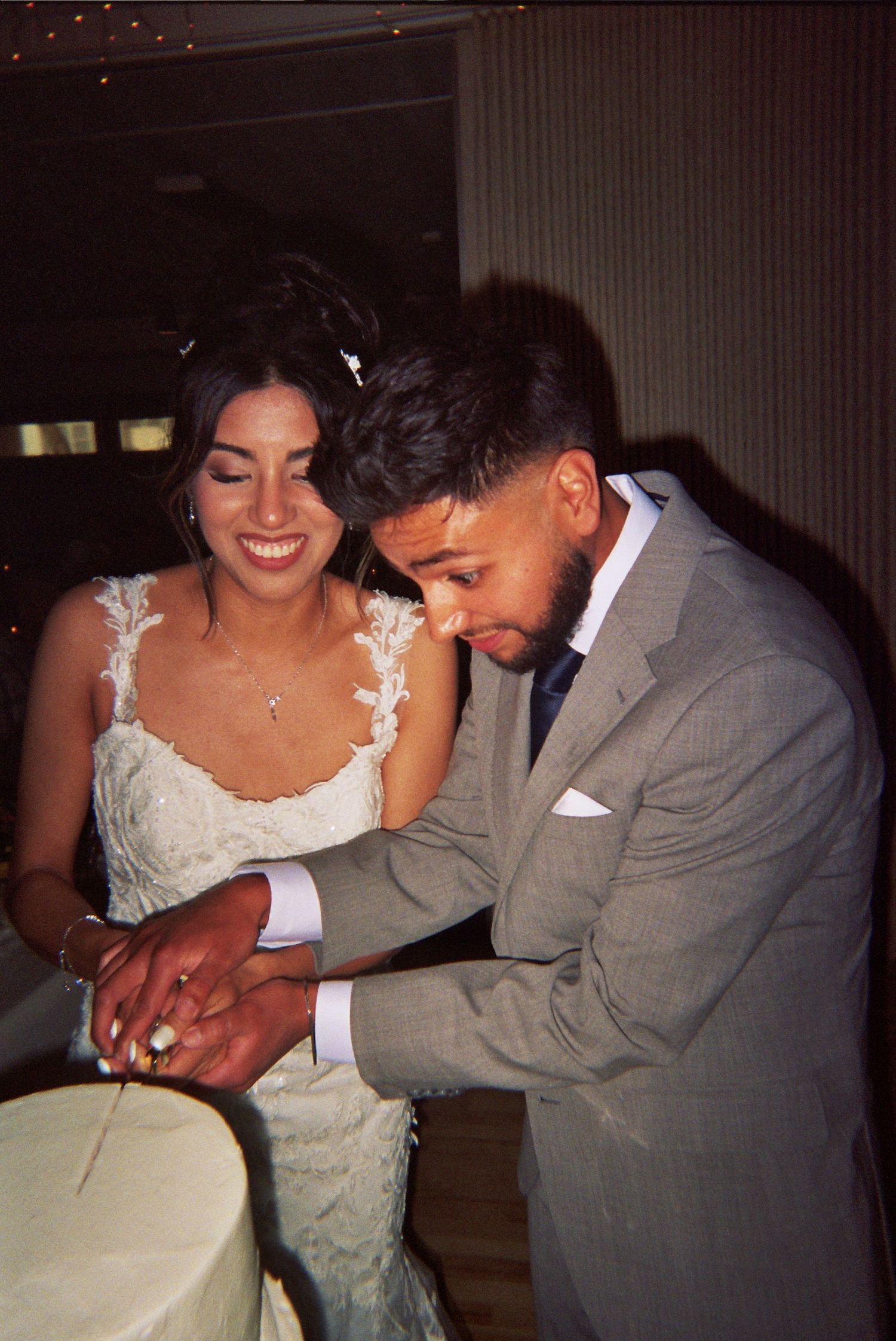A bride and groom share a joyful moment while cutting their wedding cake together at their reception.