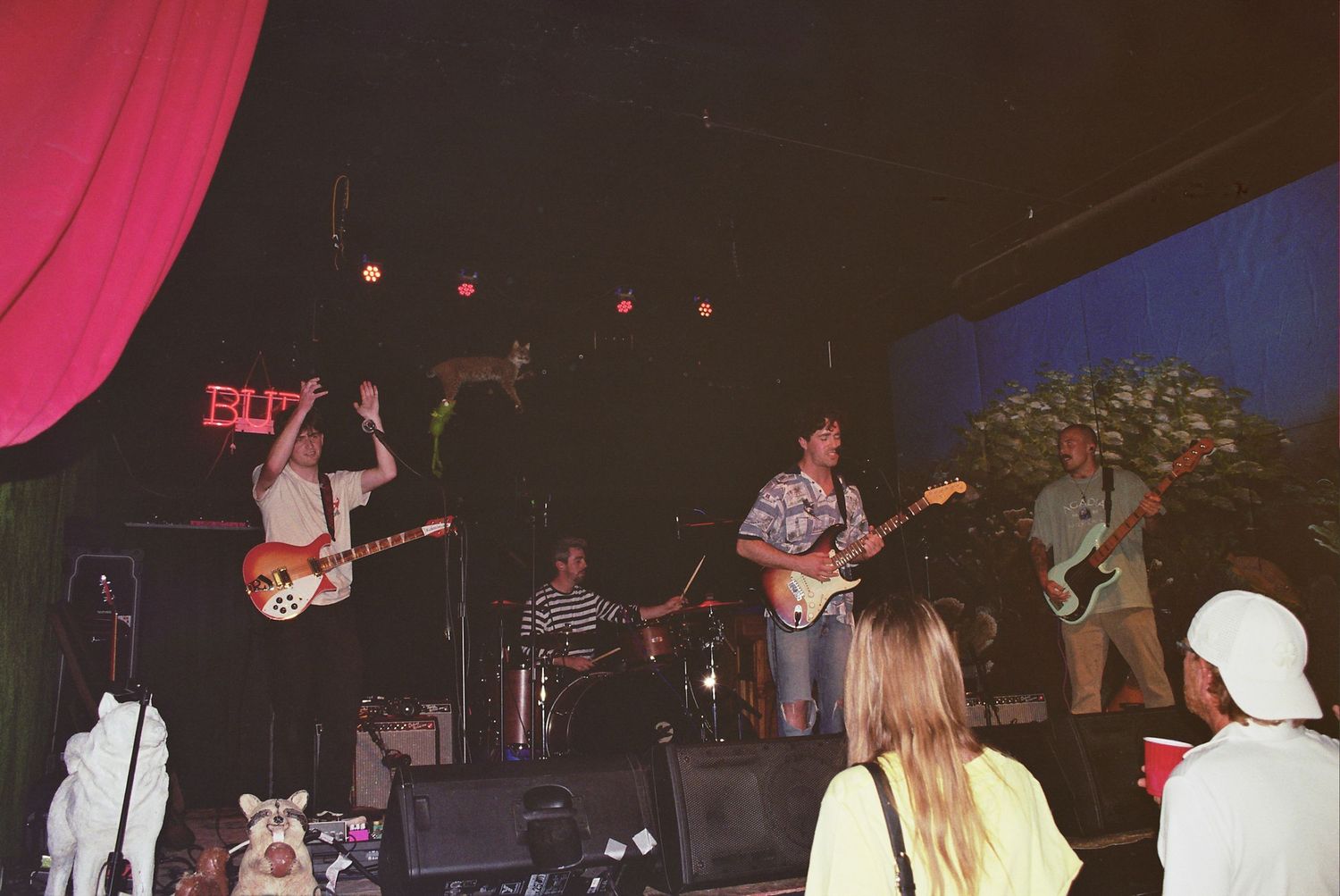 Live band performing on stage at a dimly lit music venue with audience members watching in the foreground.