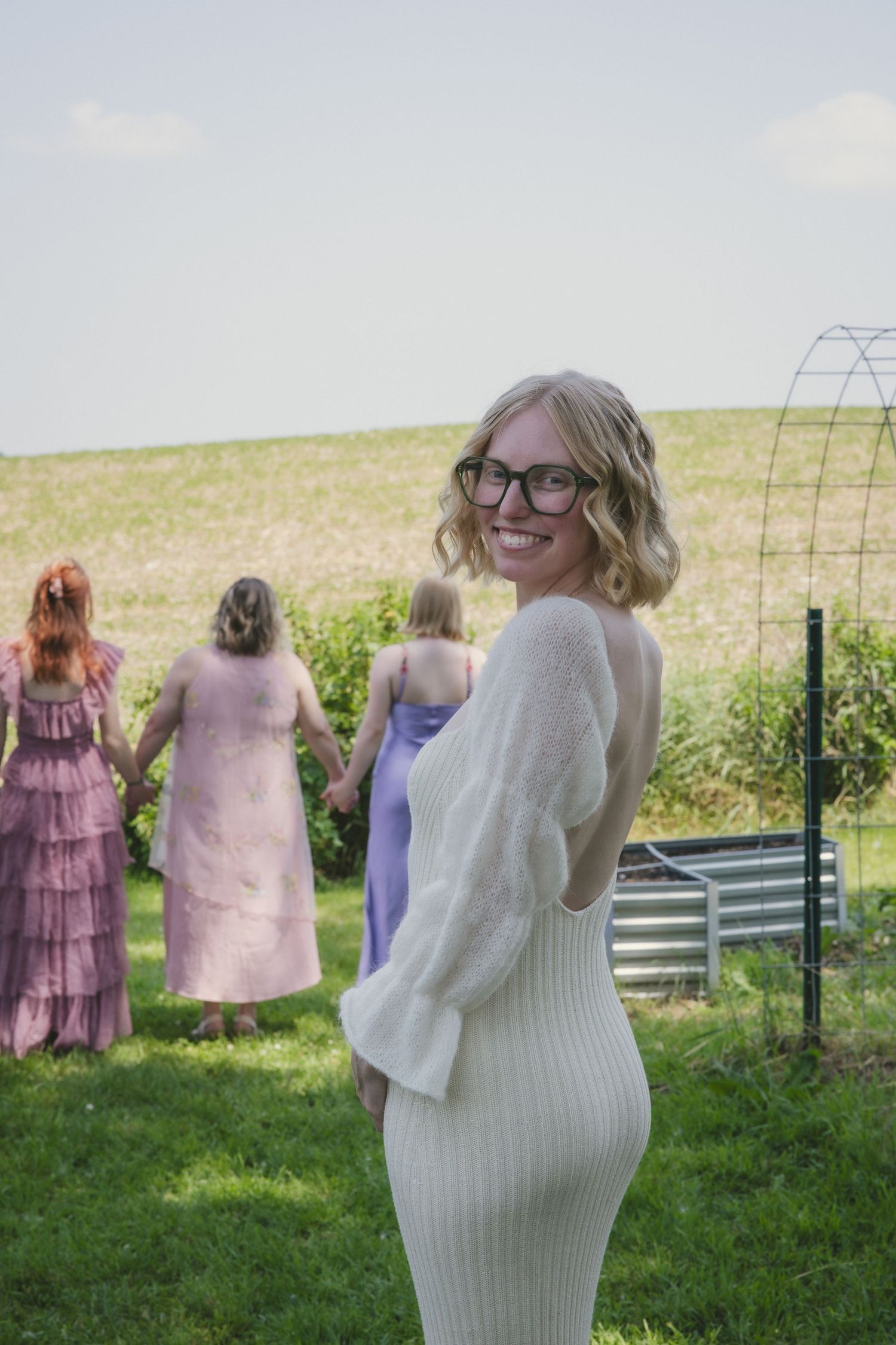 People standing in a grassy field on a sunny day wearing dresses and sweaters.