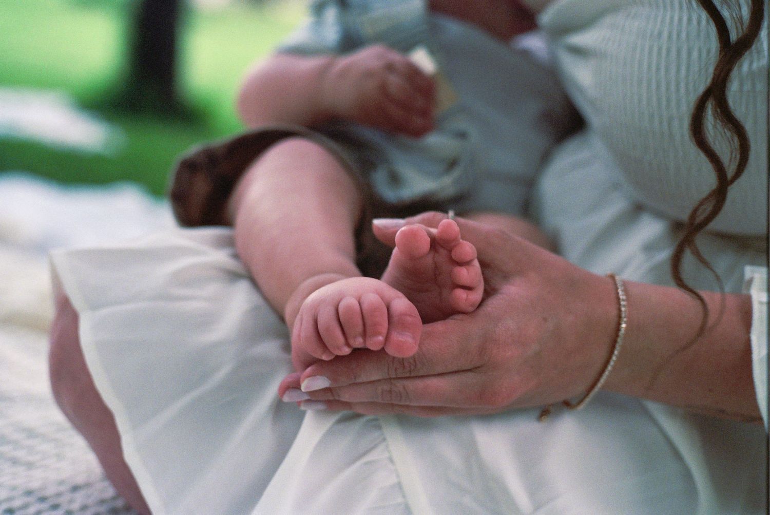 Small baby feet resting in adult hands while wearing white fabric clothing.