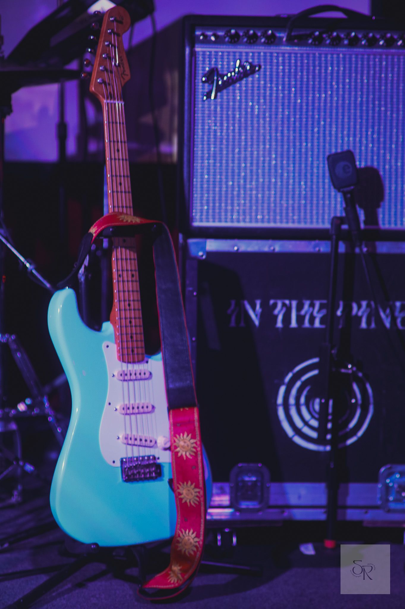 Teal electric guitar captured in progressive movement shots against a dark purple stage backdrop with amplifiers.