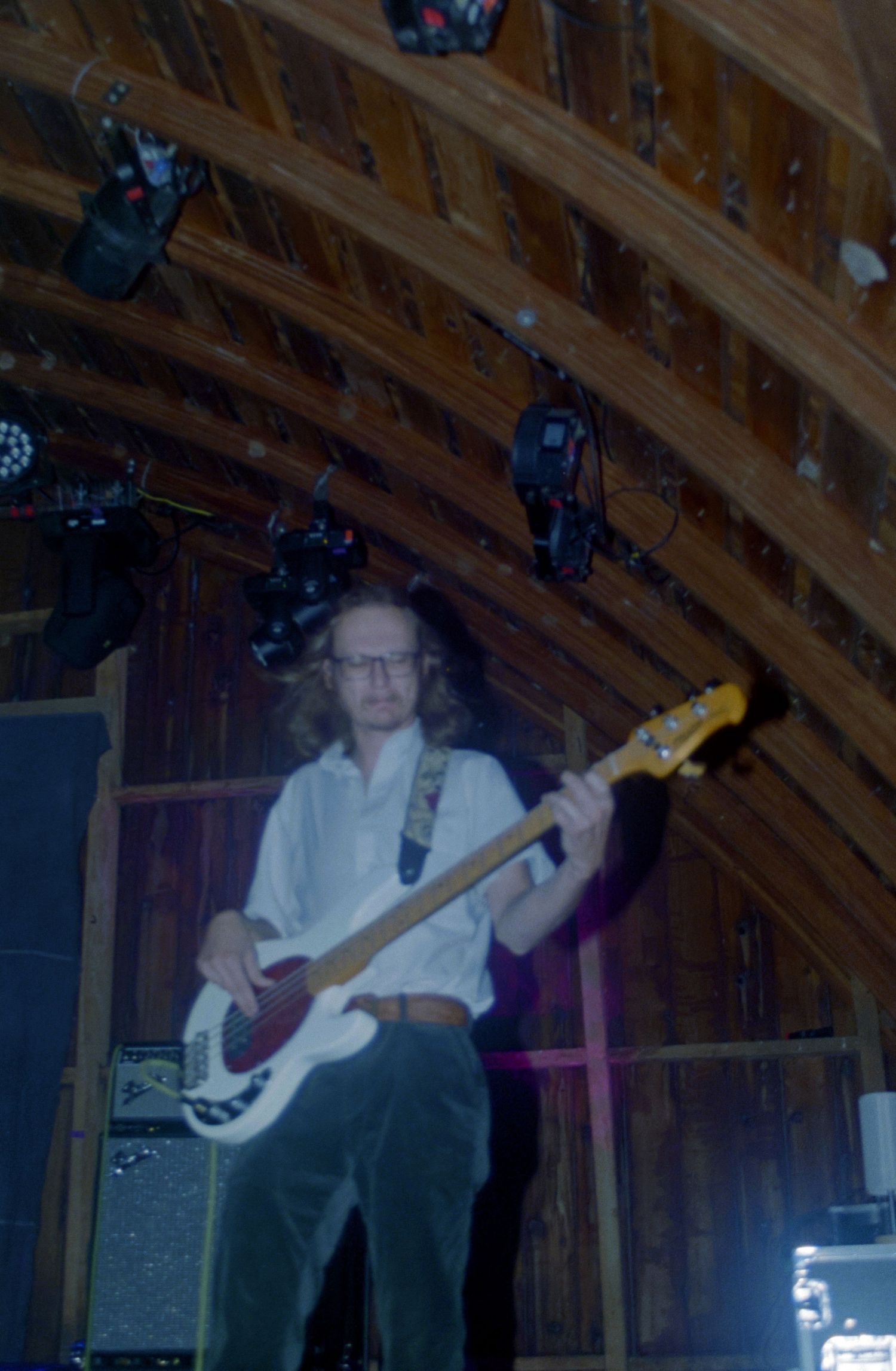 Musician playing electric guitar on stage in a wooden barn venue with stage lighting overhead.