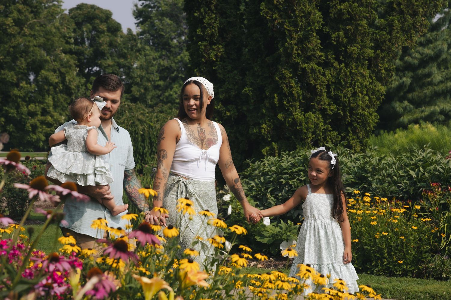 Family strolling through a vibrant garden with colorful flowers, parents holding children on a sunny day.