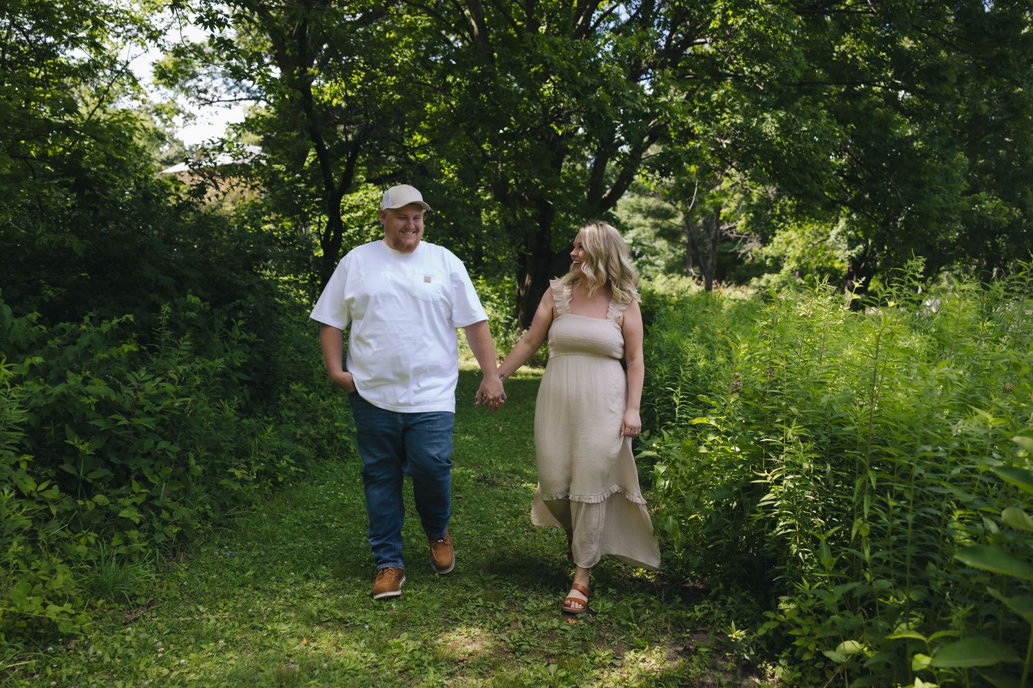 Couple holding hands walking on a lush green nature path surrounded by trees on a sunny day.