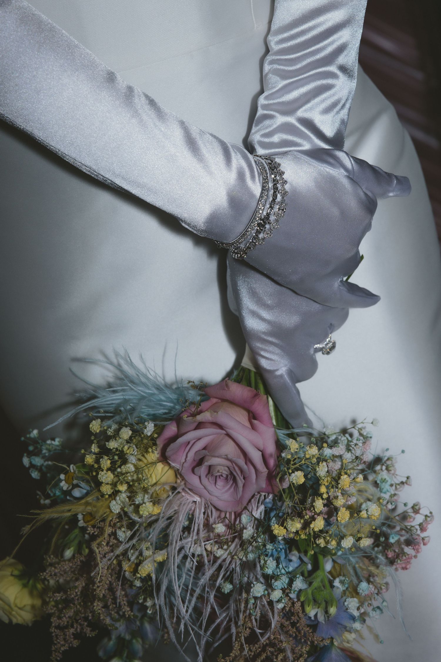 Close-up sequence of a white satin sleeve with decorative rhinestone details next to delicate pink and yellow flowers.