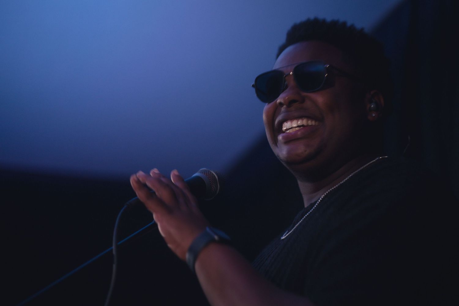 Stage performer singing into microphone under blue lighting during concert performance.