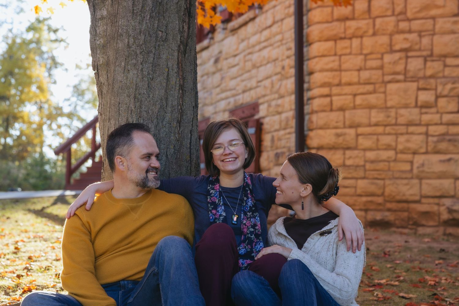 A group poses together outdoors against a rustic brick wall on an autumn day.