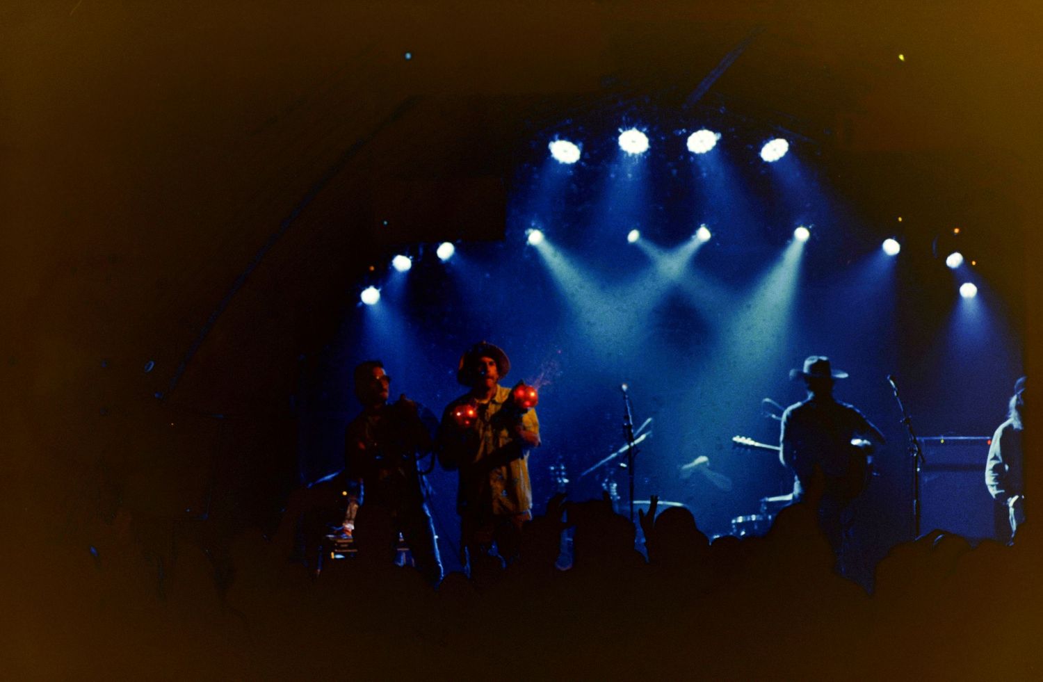 Band performing on stage under blue spotlights in a dark concert venue, silhouetted against dramatic lighting.