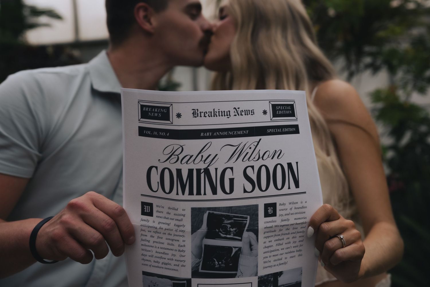 Couple kissing while holding a newspaper pregnancy announcement reading Baby Wilson Coming Soon.