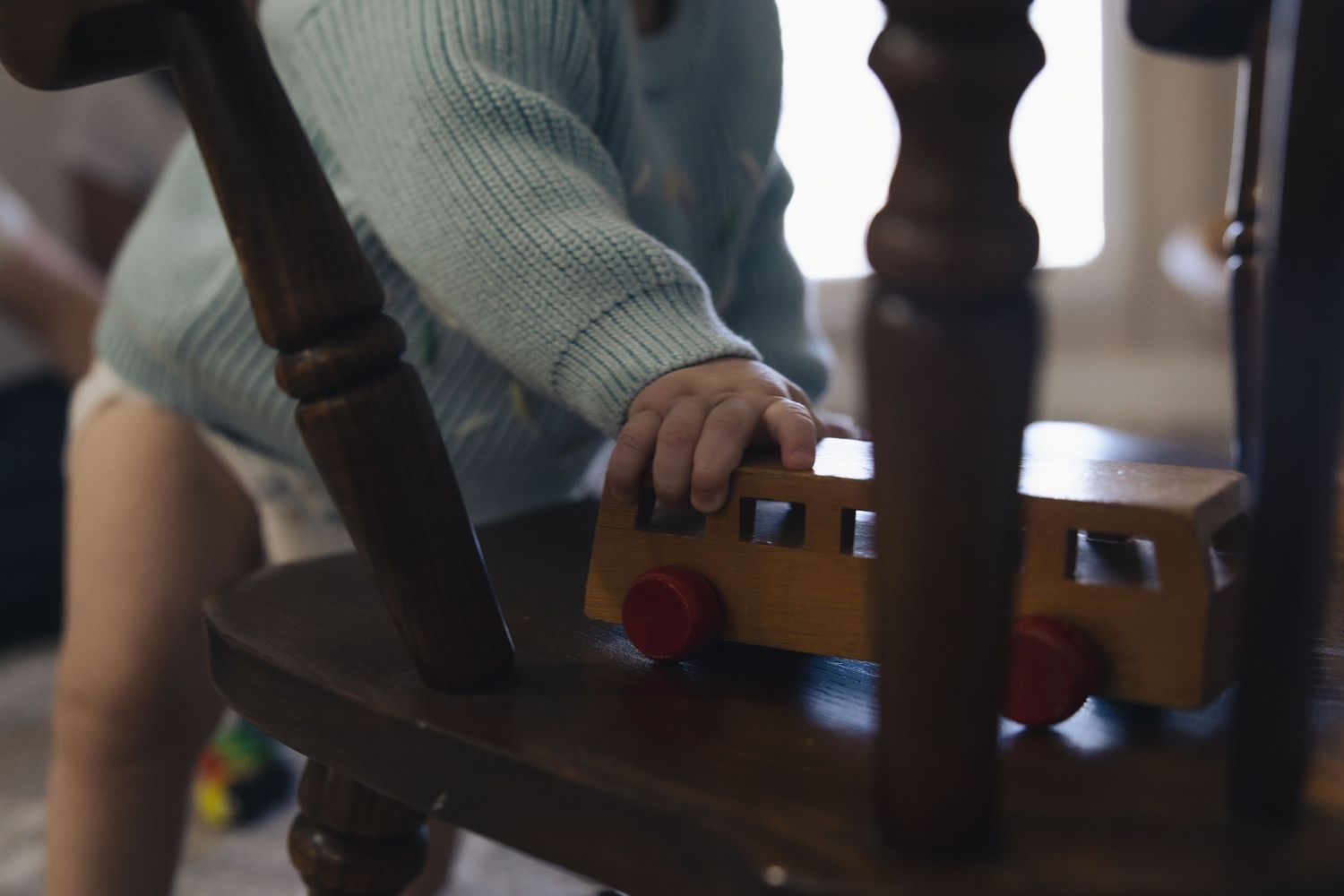 Child playing with a wooden toy bus on a chair, enjoying imaginative play in a cozy indoor setting.