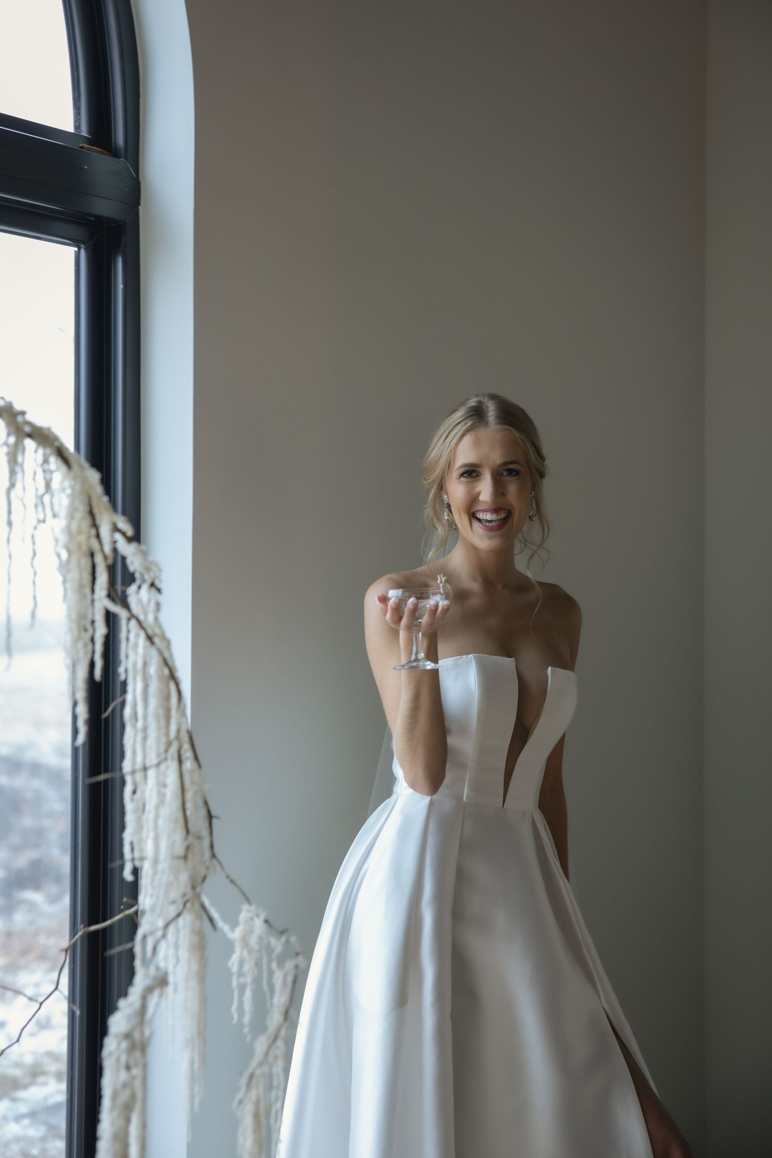 Elegant bride in a classic white off-shoulder ballgown poses by a window with natural light.