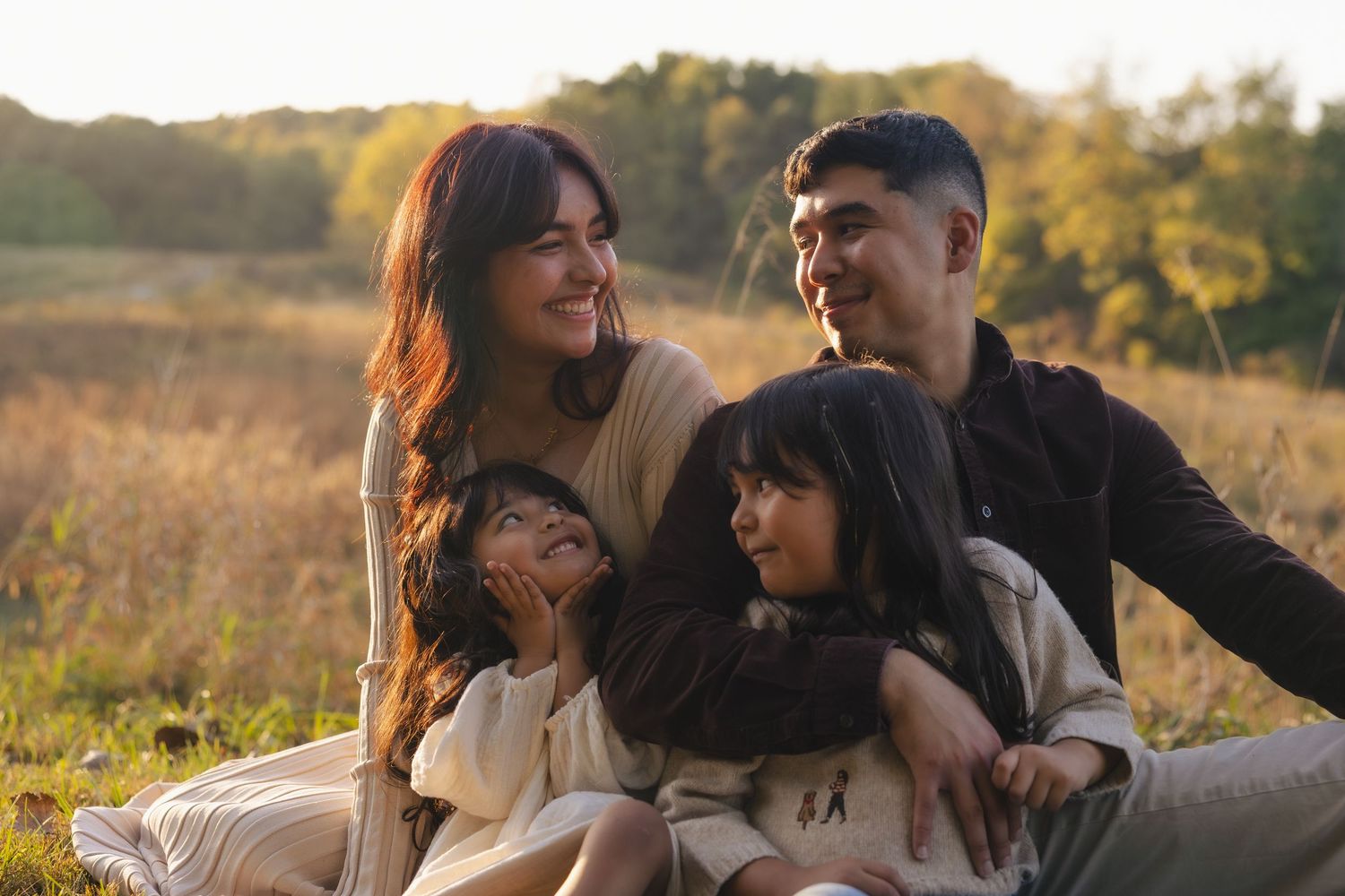 A couple shares tender moments together in a golden field during sunset as they embrace and laugh together.