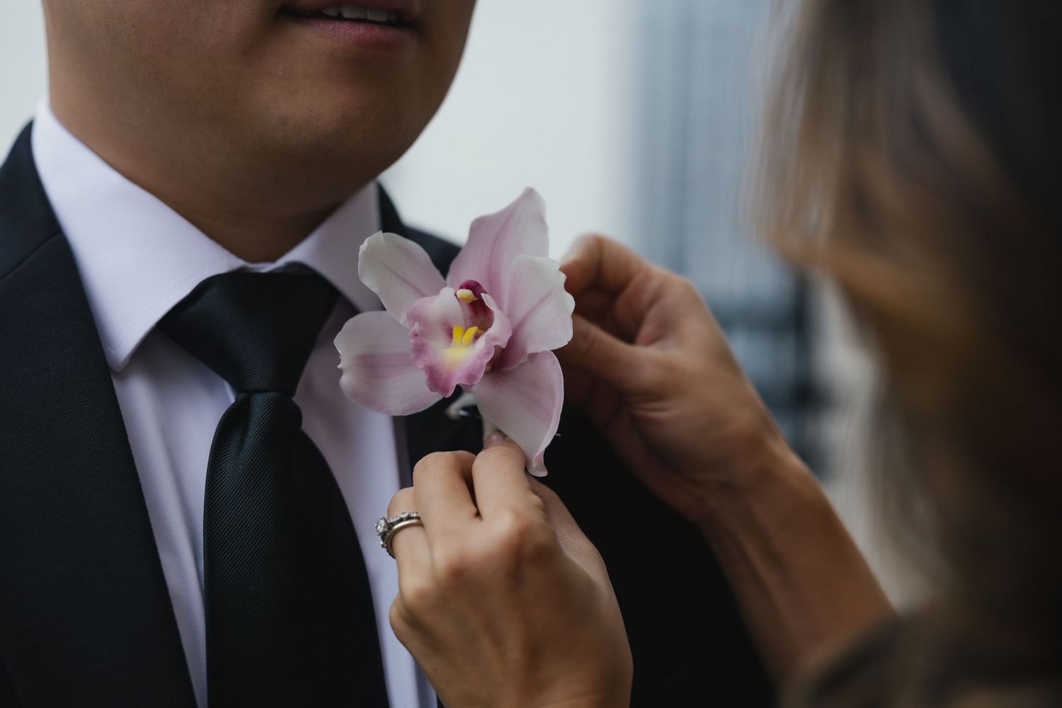 Hand adjusting a pink orchid boutonniere on a black suit lapel for a formal occasion.