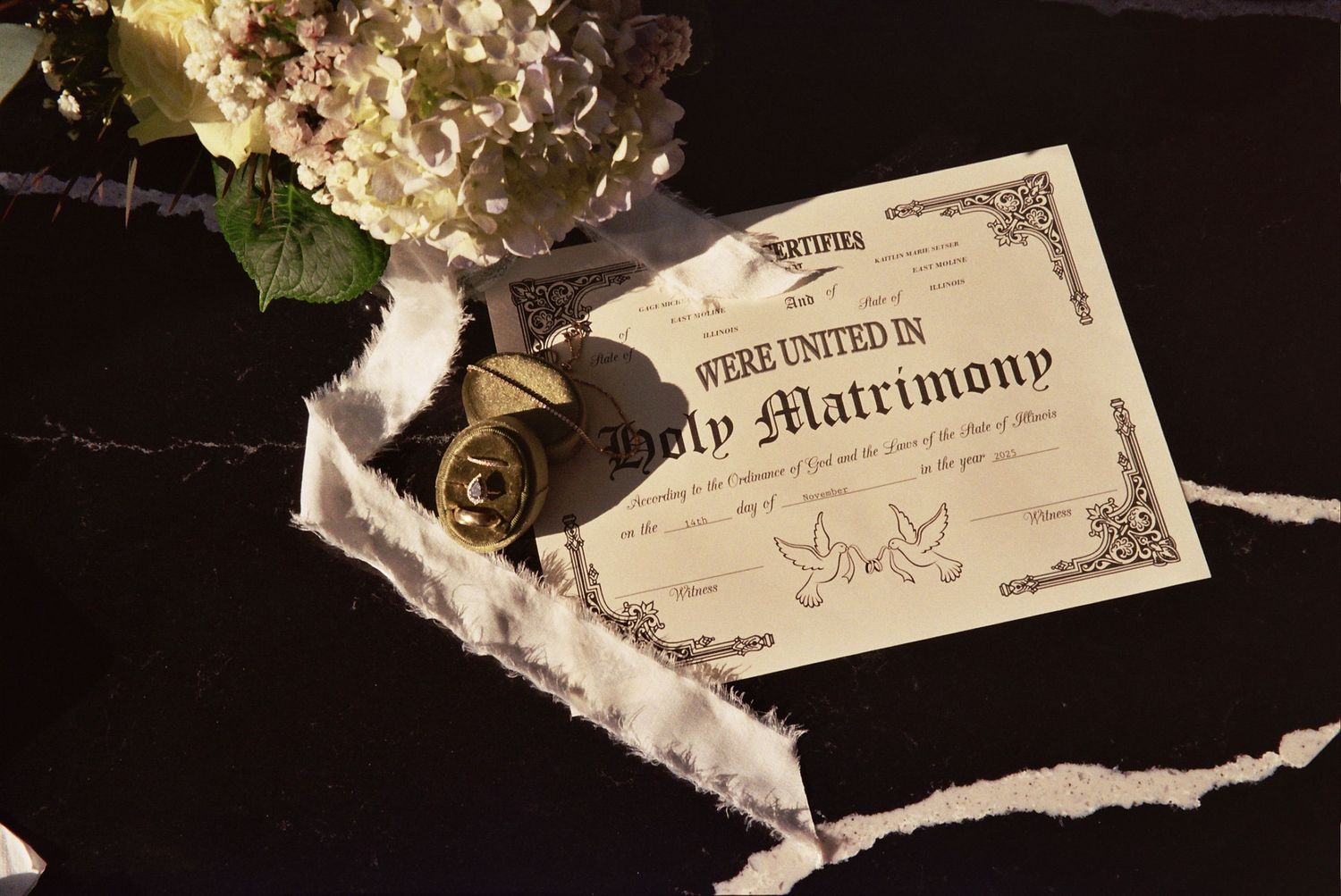 Holy matrimony certificate with wedding rings and white hydrangea flowers on dark background.