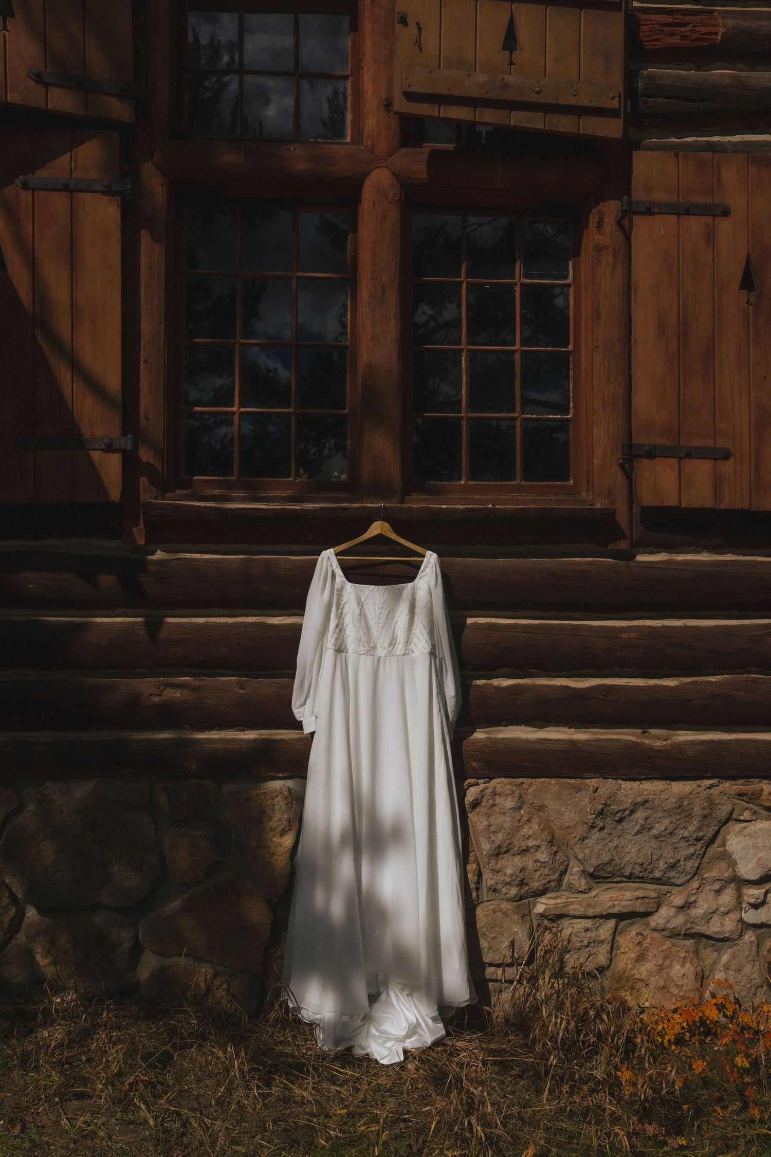 White wedding dress hanging on rustic wooden wall in moody lighting creates ethereal atmosphere.