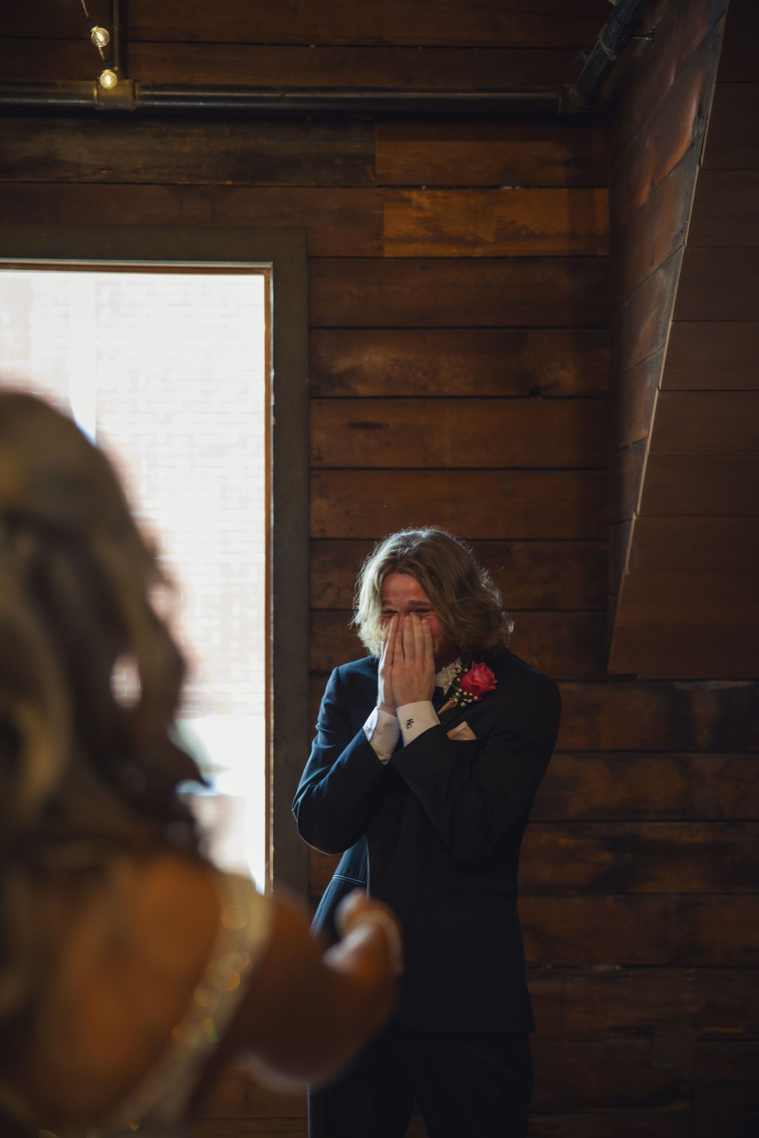 Person holding their face with both hands in a wooden cabin interior with warm lighting and window.