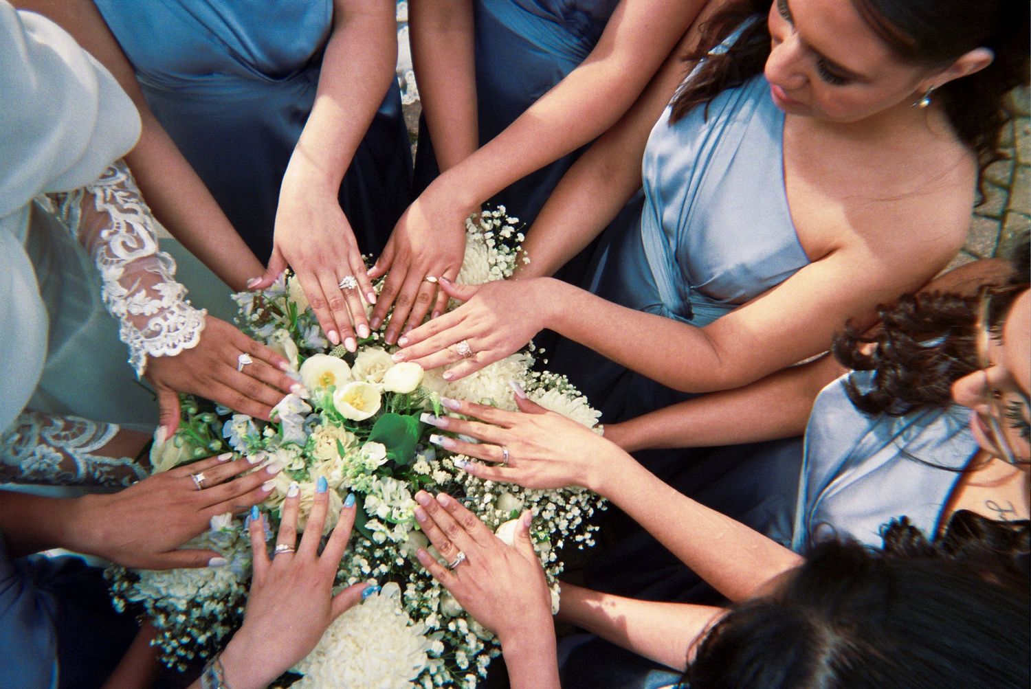 Group of hands gathered in a circle holding delicate white baby's breath flowers and pale blue bridesmaid dresses.