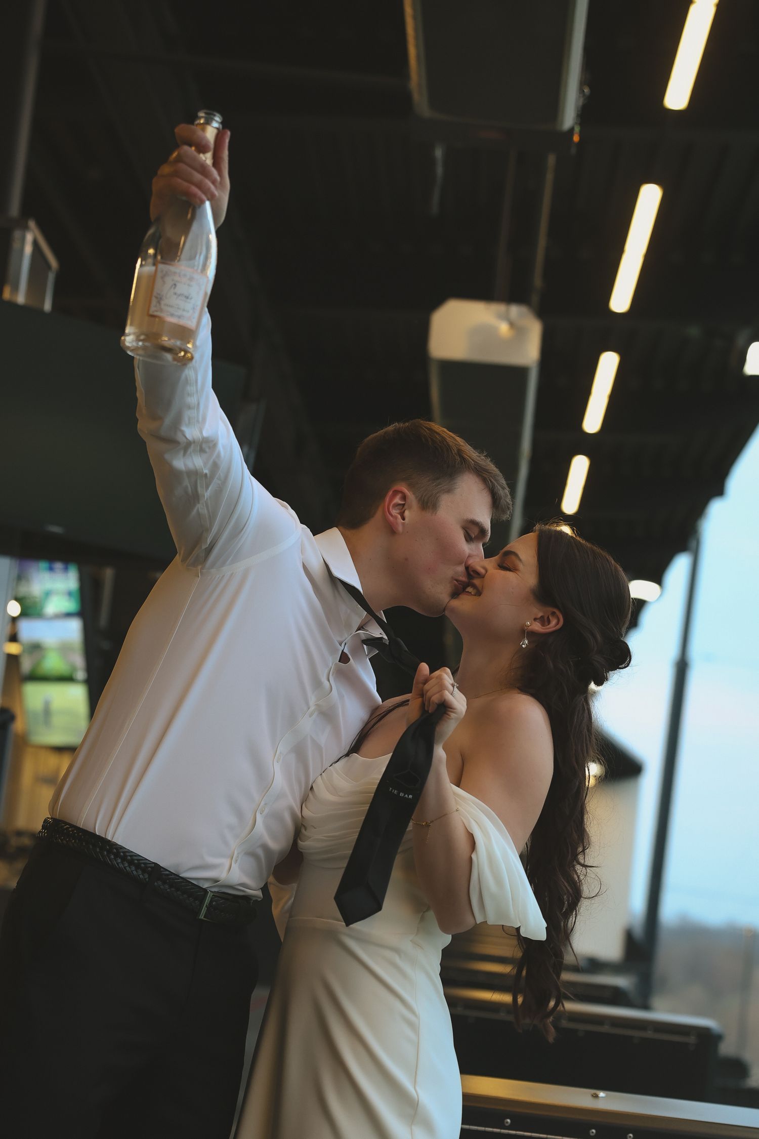 A romantic couple shares a passionate kiss on their wedding day as they dance in an indoor venue.