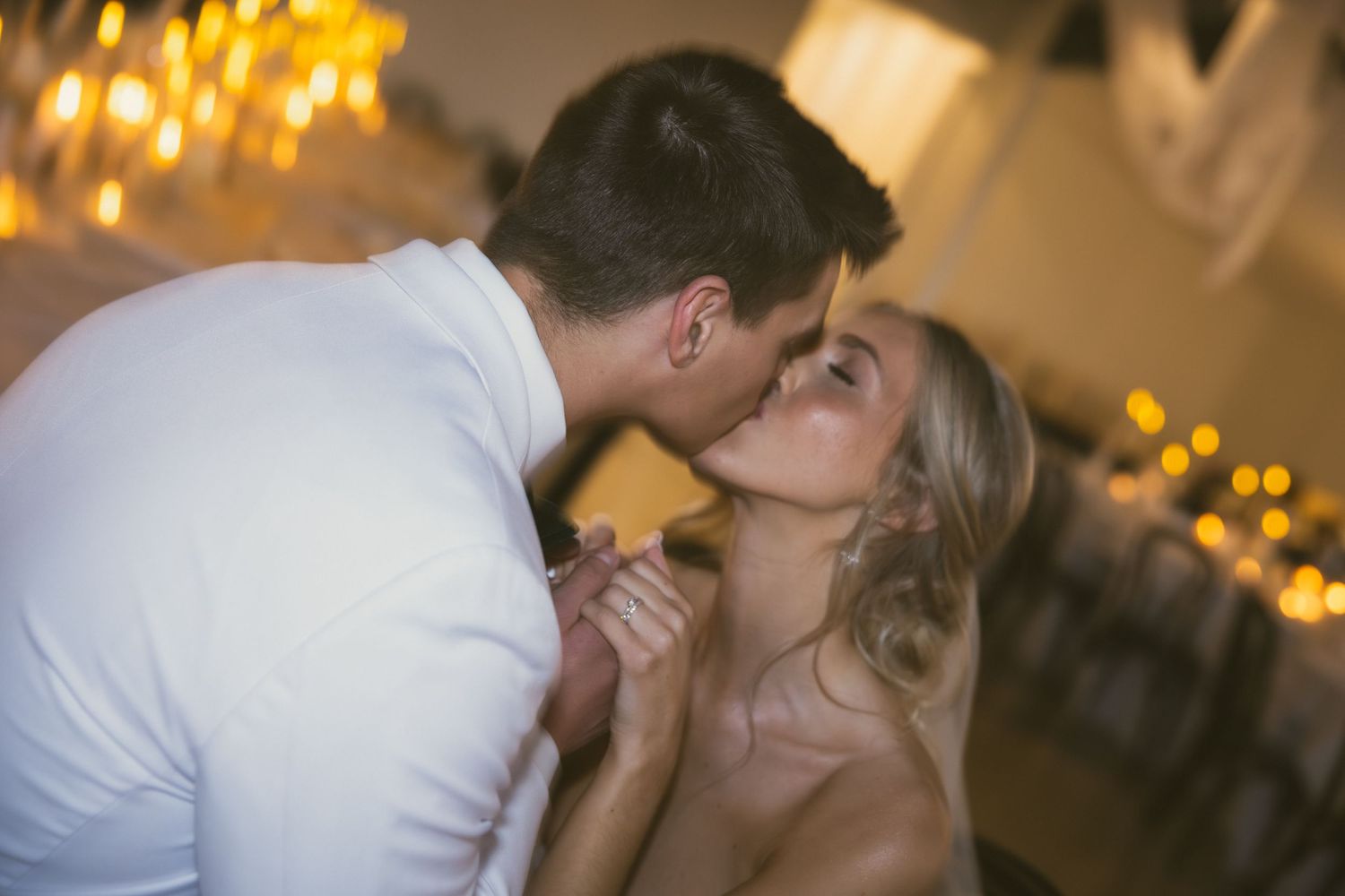 A romantic kiss between newlyweds with soft golden lighting in the background.