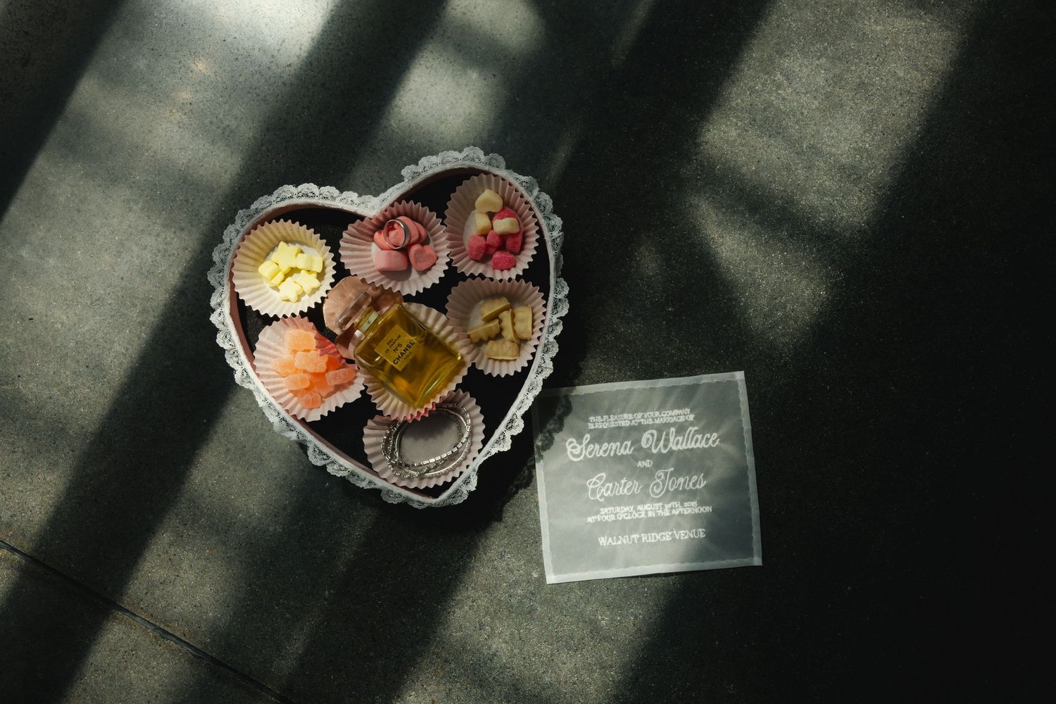 A heart-shaped crystal dish filled with colorful macarons sits beside a small glass plaque on a dark surface.