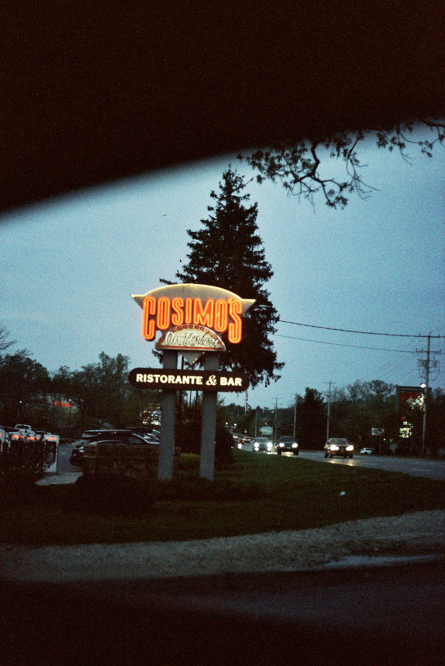 Illuminated vintage sign for Cosimo's restaurant and bar glows against a twilight sky with pine trees.