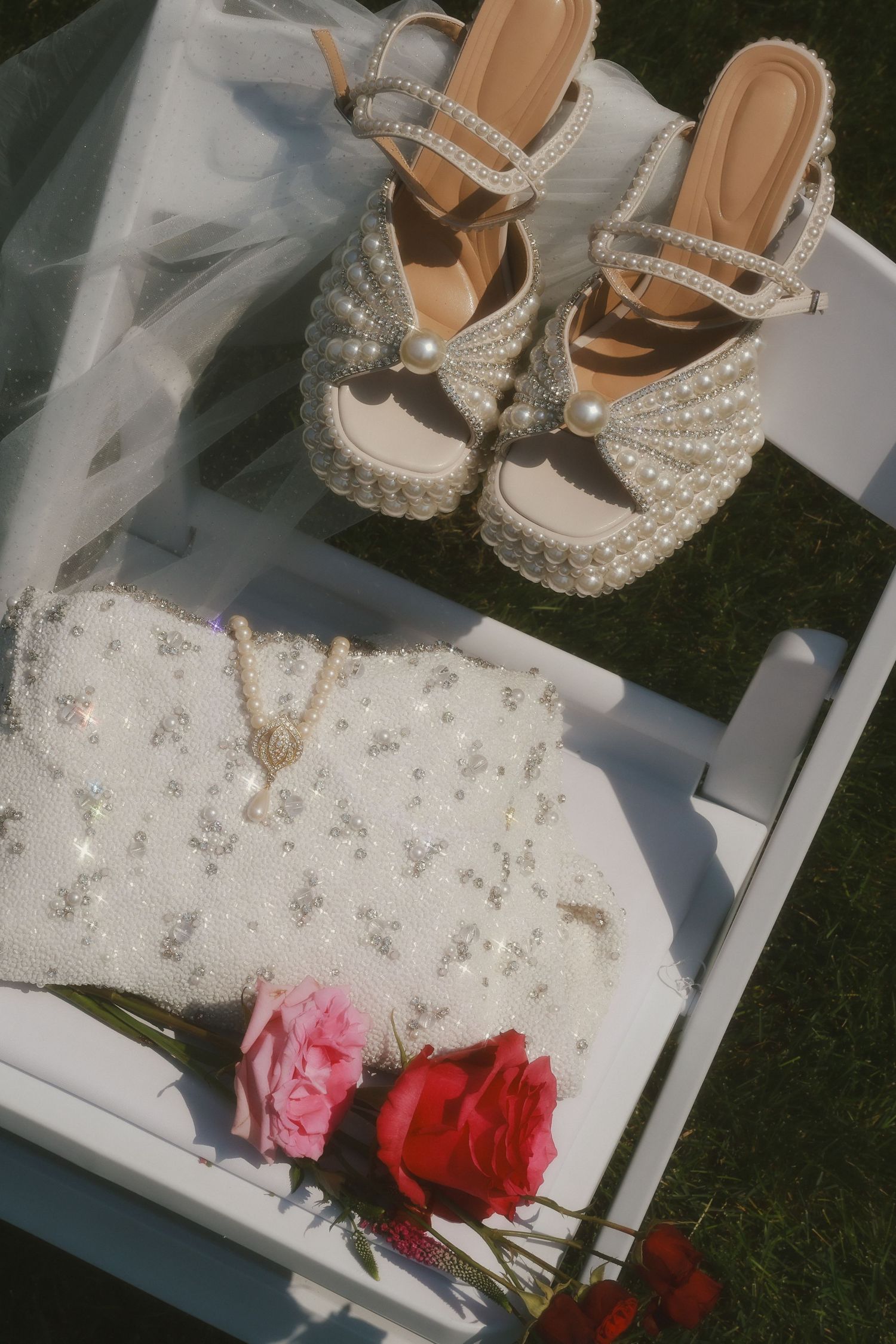 Pearl embellished wedding shoes displayed on white chair with delicate pink and red floral accents.