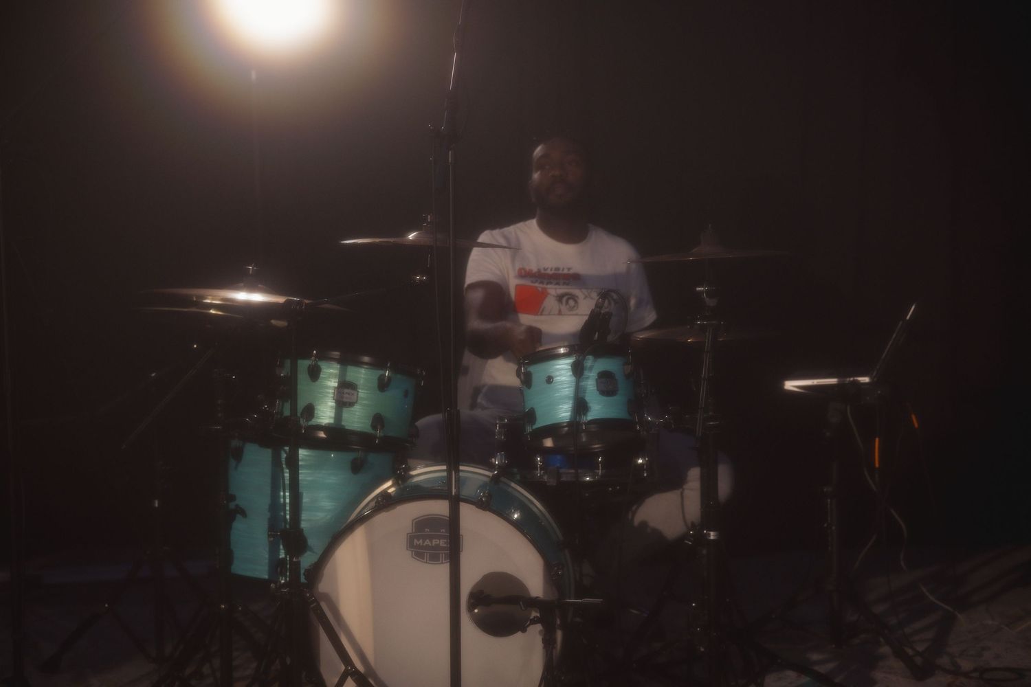 Drummer performs on stage with dramatic backlighting and a drum kit in a dark concert setting.