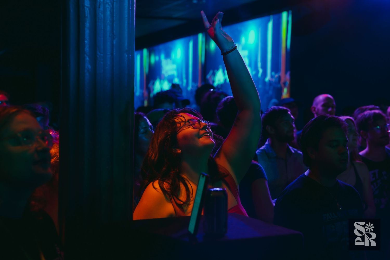 Concert attendees dance and celebrate at a nightclub illuminated by vibrant blue lighting.