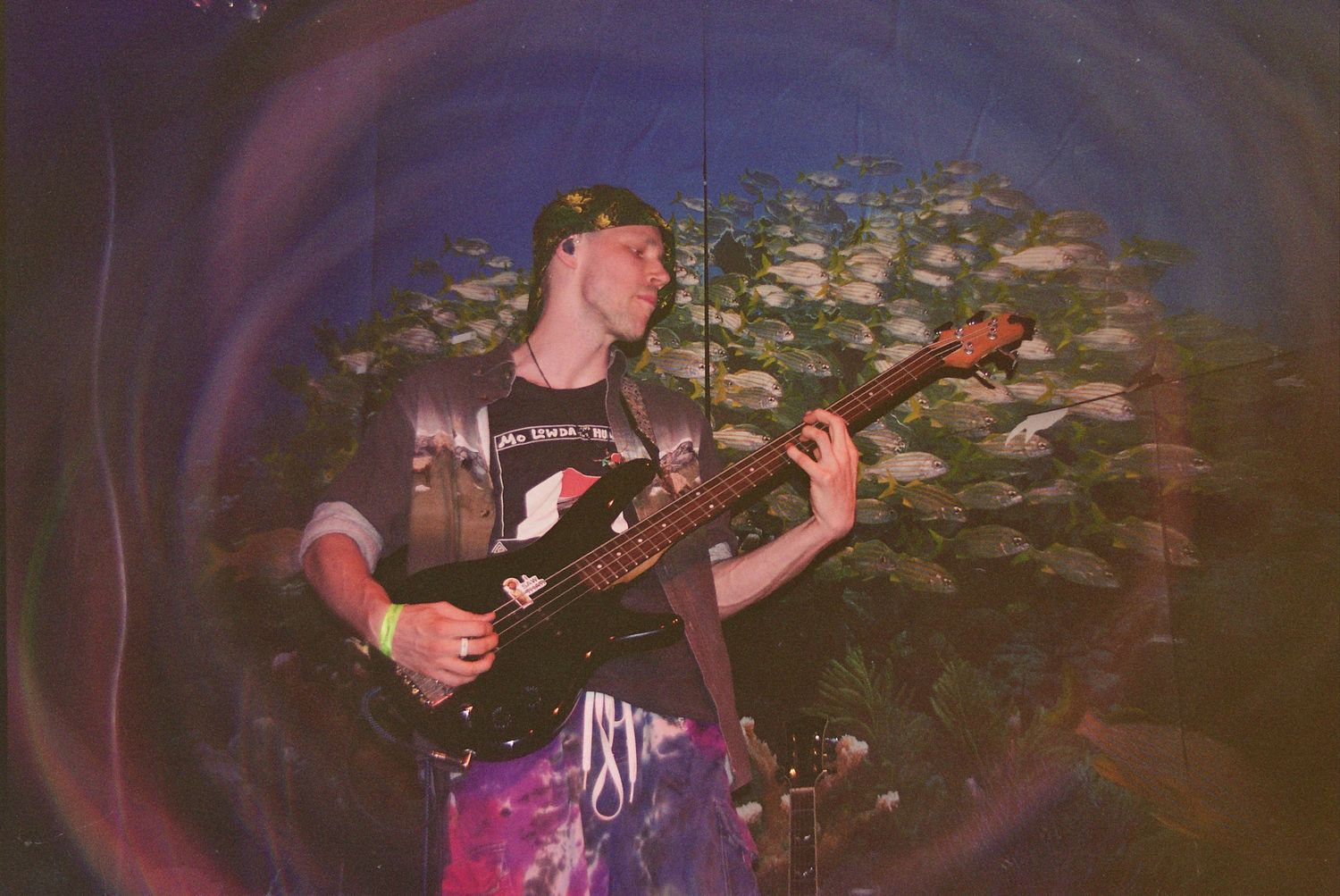 Young guitarist playing black electric guitar outdoors at night with colorful psychedelic light effects.