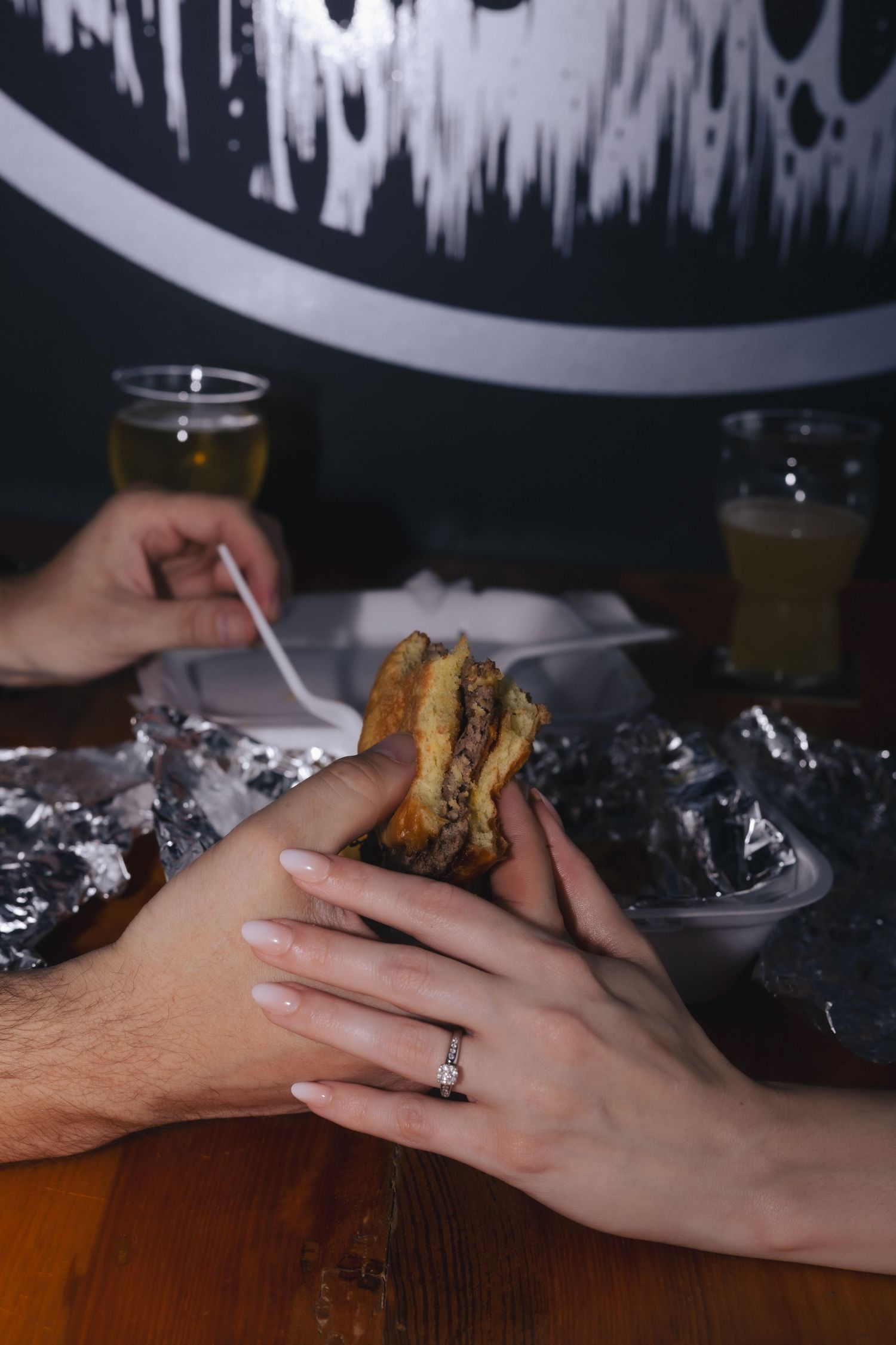 Couple sharing a burger together at a restaurant table, with drinks and foil wrappers visible nearby.