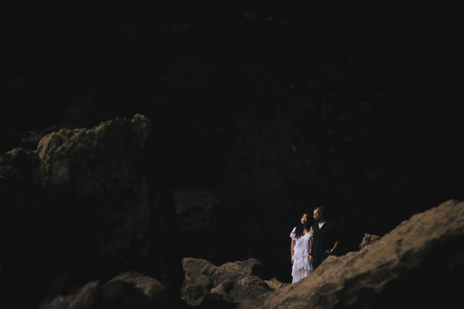 Romantic couple sharing intimate moment on rocky terrain with rustic desert landscape in background.