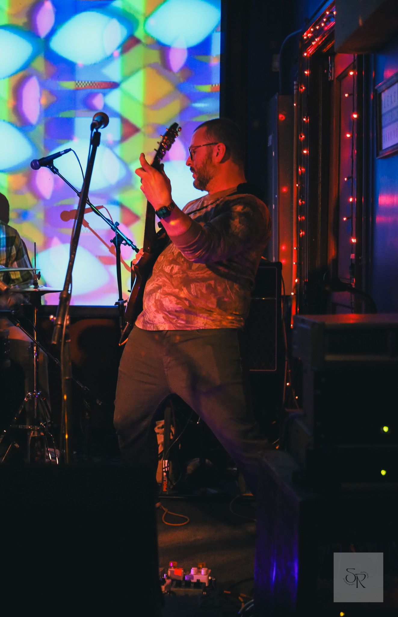 A performer sings on stage at a music venue with colorful bokeh lights creating a vibrant backdrop behind them.