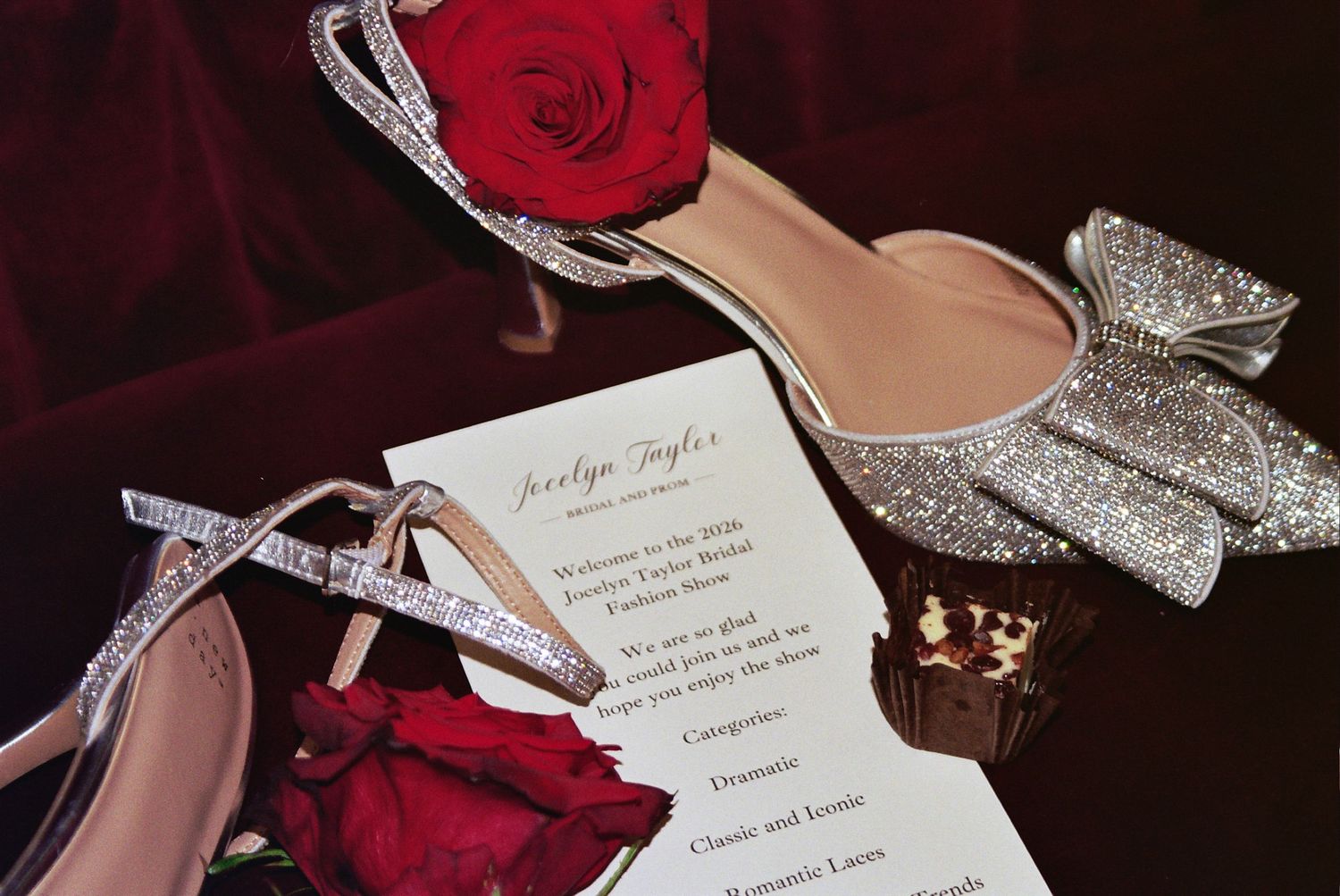Elegant bridal flat lay featuring crystal embellished heels, glitter bow pumps, red roses, and a wedding program on velvet.