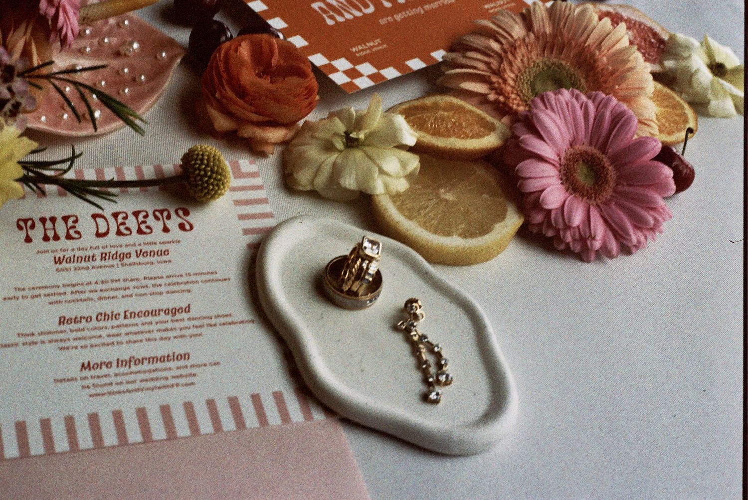 Small ceramic jewelry dish with earrings alongside pink florals and vintage paper decor on a white surface.