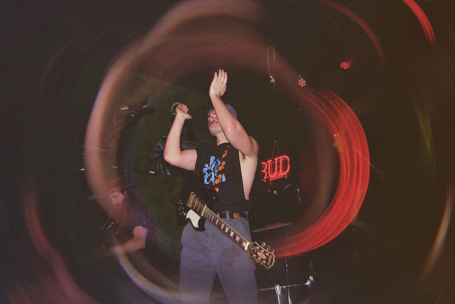 Guitarist performing on stage with dynamic light trails and a Budweiser sign glowing in the background.