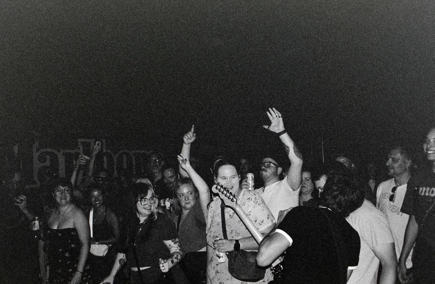 Black and white photo of a lively crowd at a concert, with people dancing and raising hands in the air.