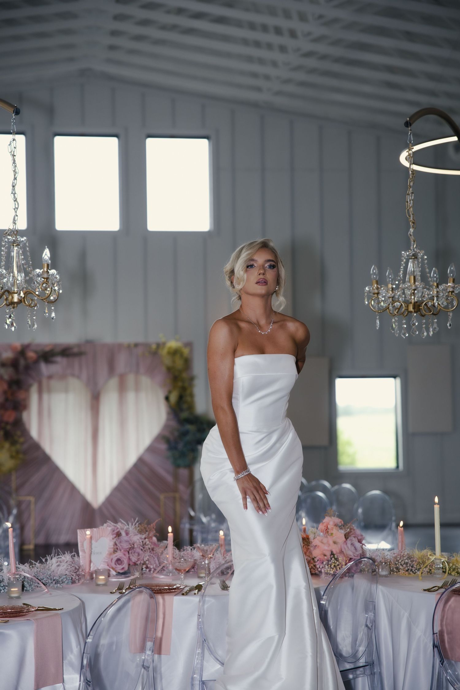 Elegant wedding reception venue with crystal chandeliers, pink decor, and a figure in a white strapless gown.