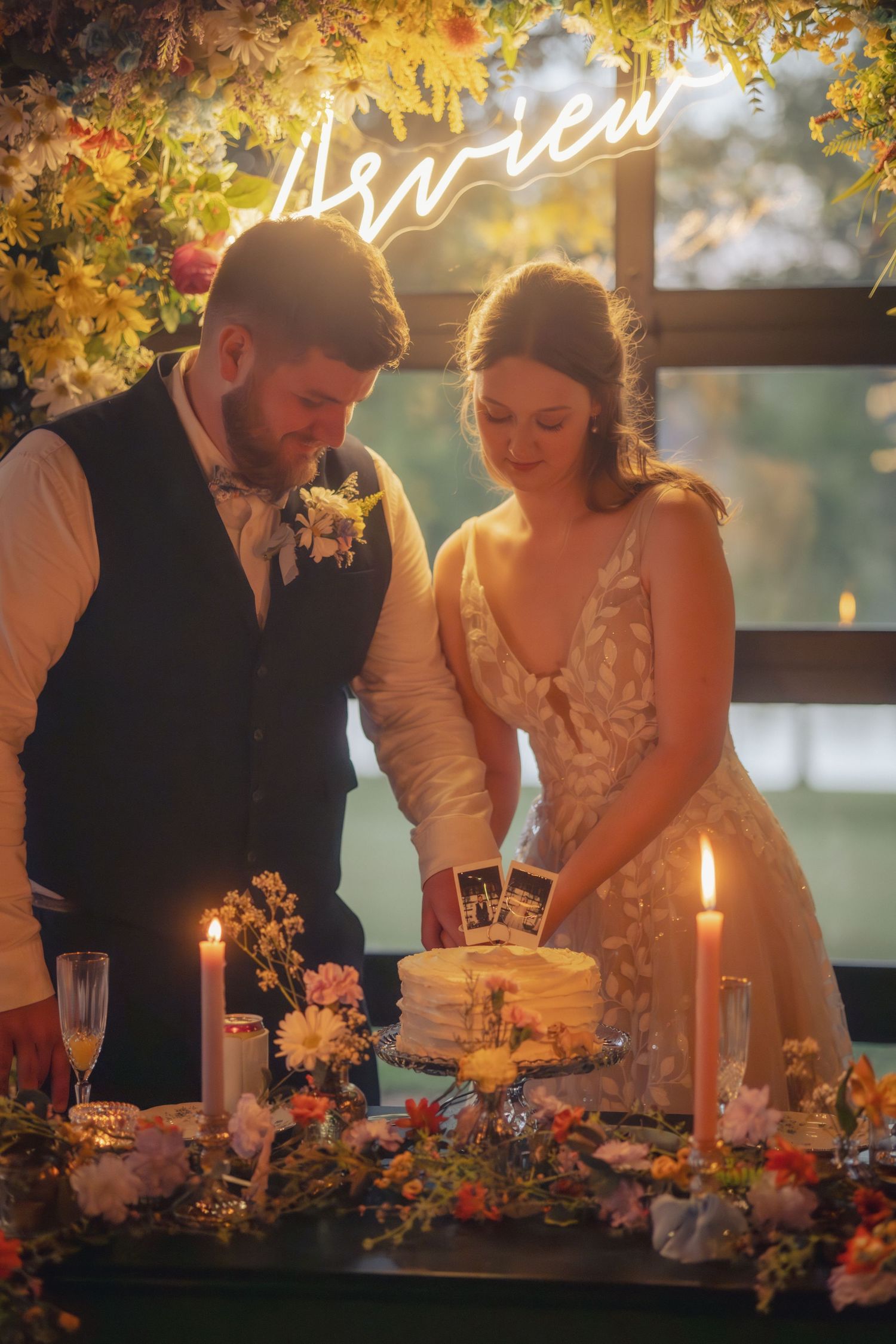Couple cutting wedding cake under glowing neon sign with autumn decorations.