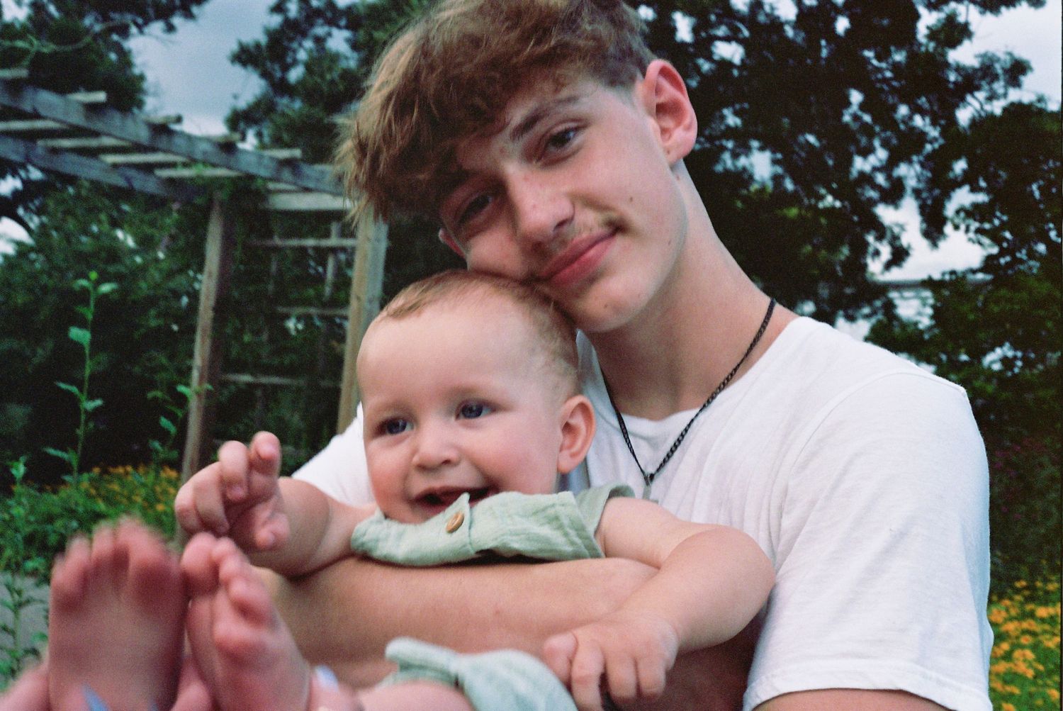 A parent and baby share a tender outdoor moment together in a lush green park setting during daytime.