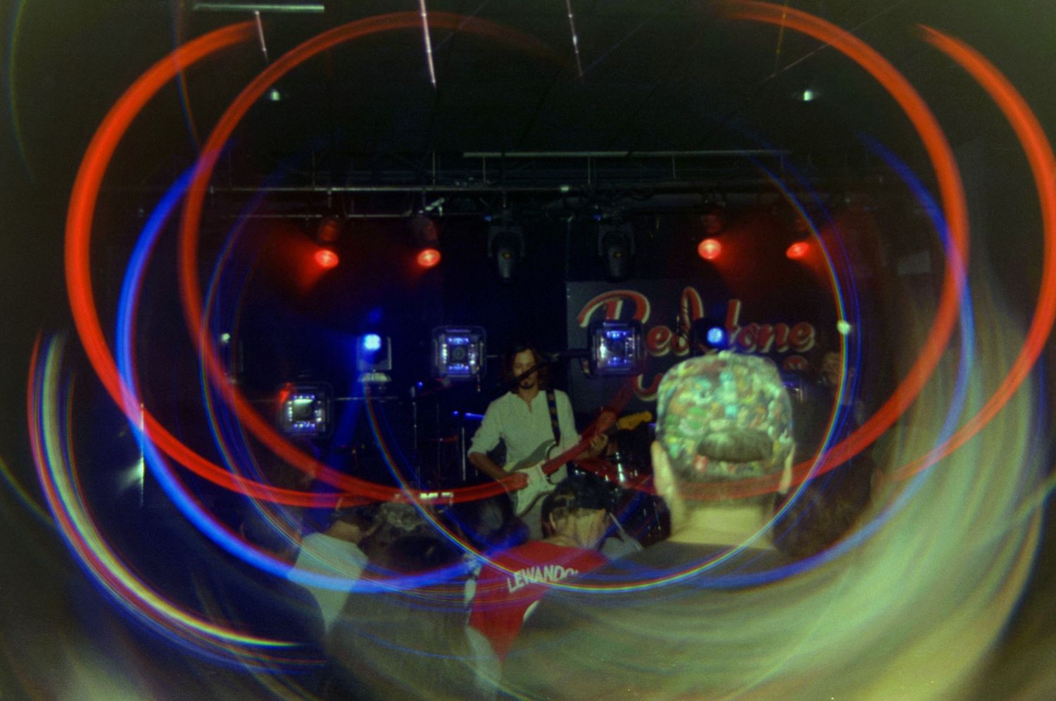 Band performing on stage with vibrant red and blue light trails swirling around musicians in a dark concert venue.
