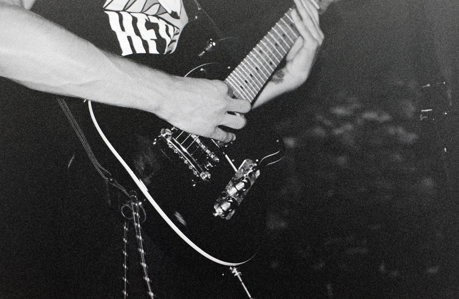 Black and white photo of a guitarist playing an electric guitar on stage during a live performance.