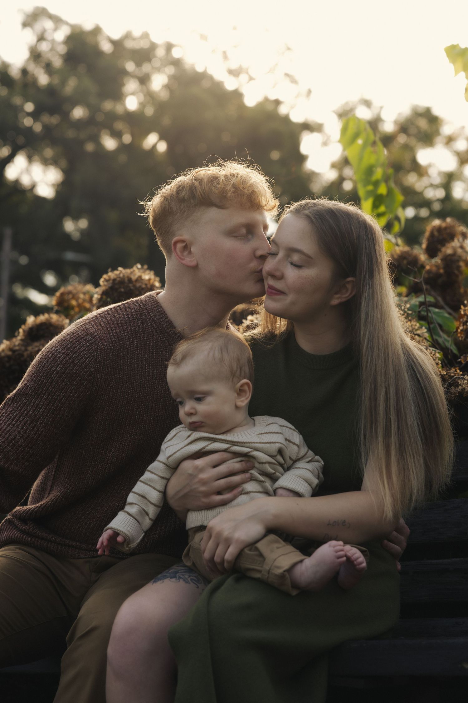 A loving family shares a tender moment together outdoors at sunset with golden light filtering through trees.