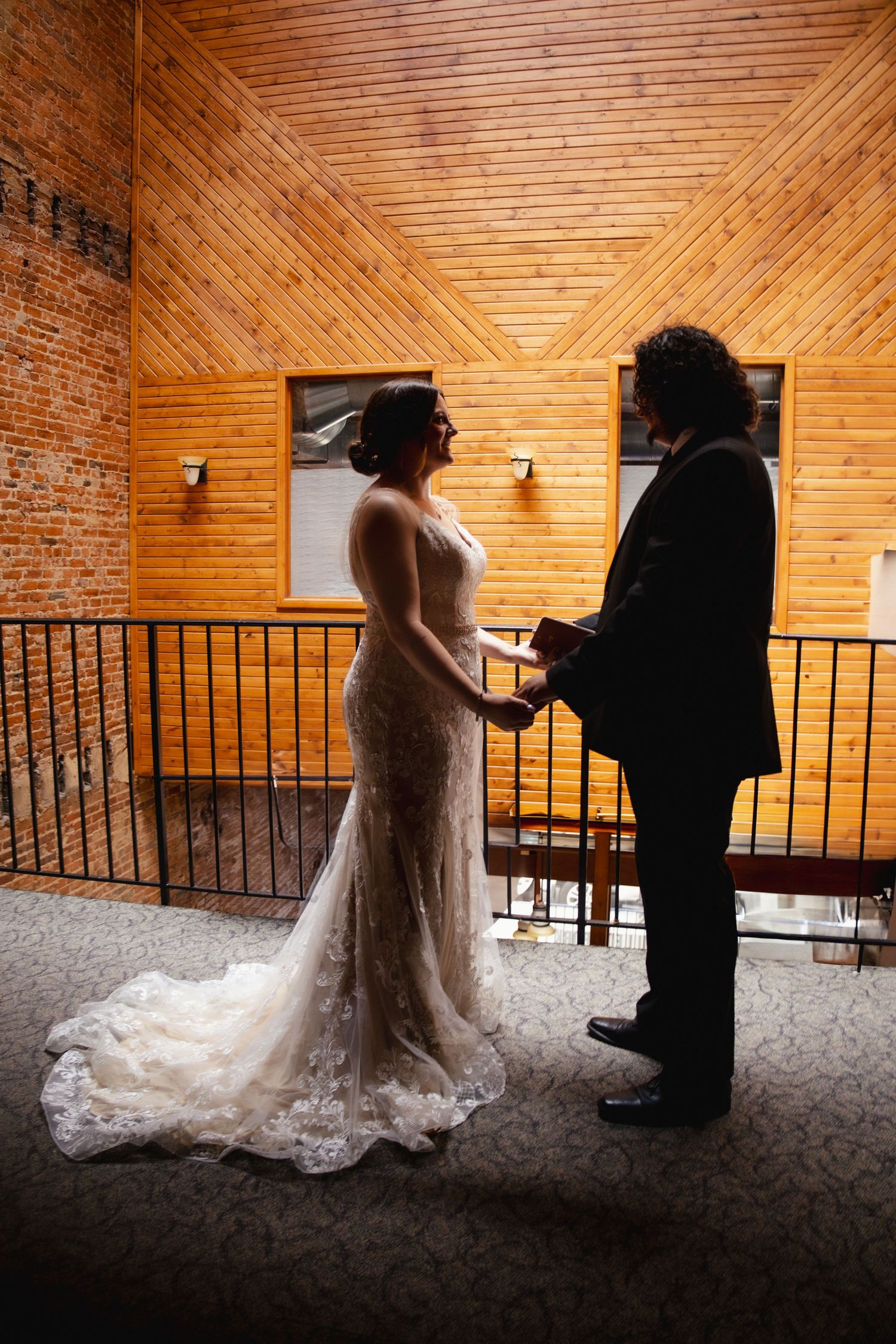 A couple stands together in a rustic venue with wood paneled walls and exposed brick during an intimate wedding ceremony.