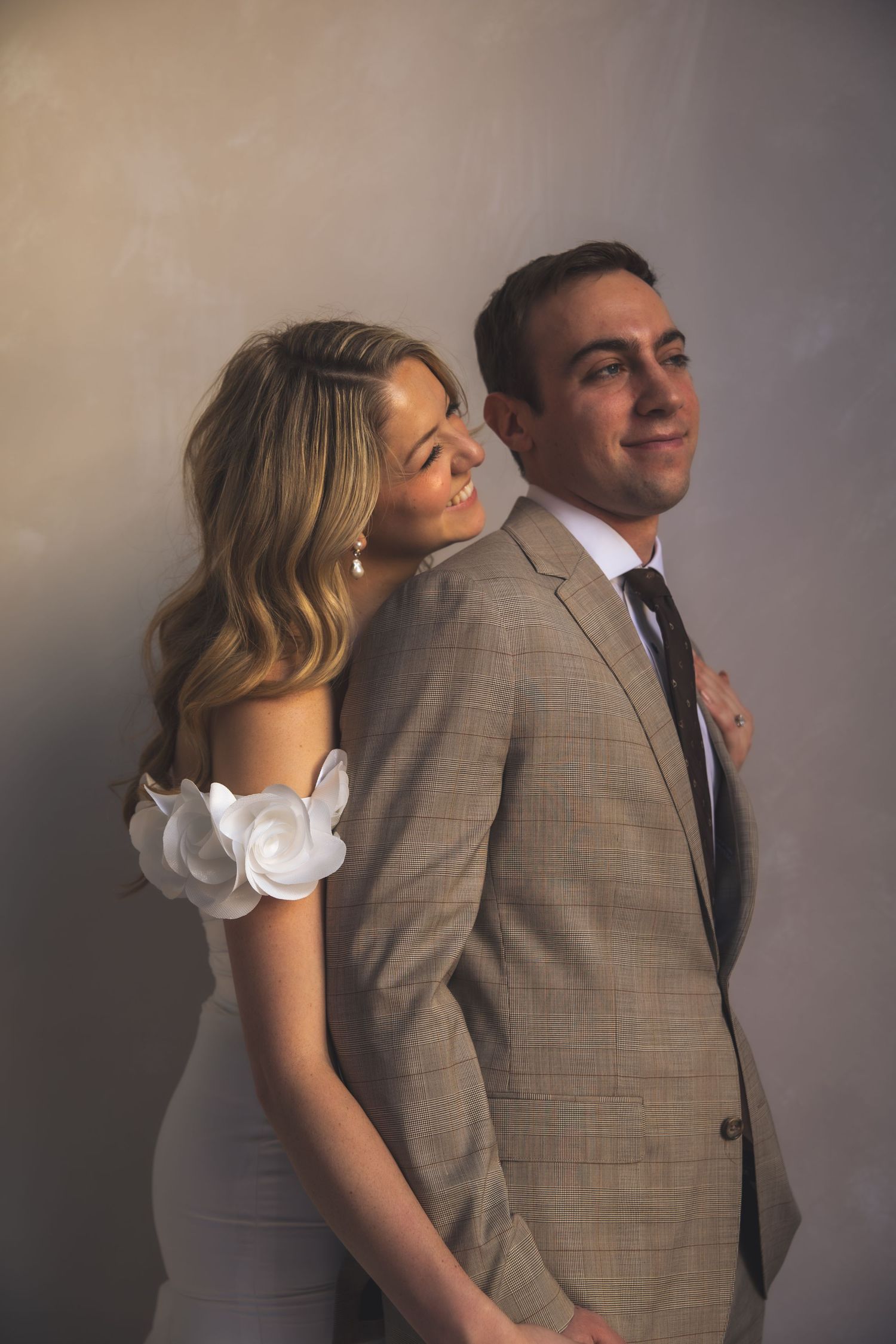 A romantic couple's portrait against a neutral wall in wedding attire.