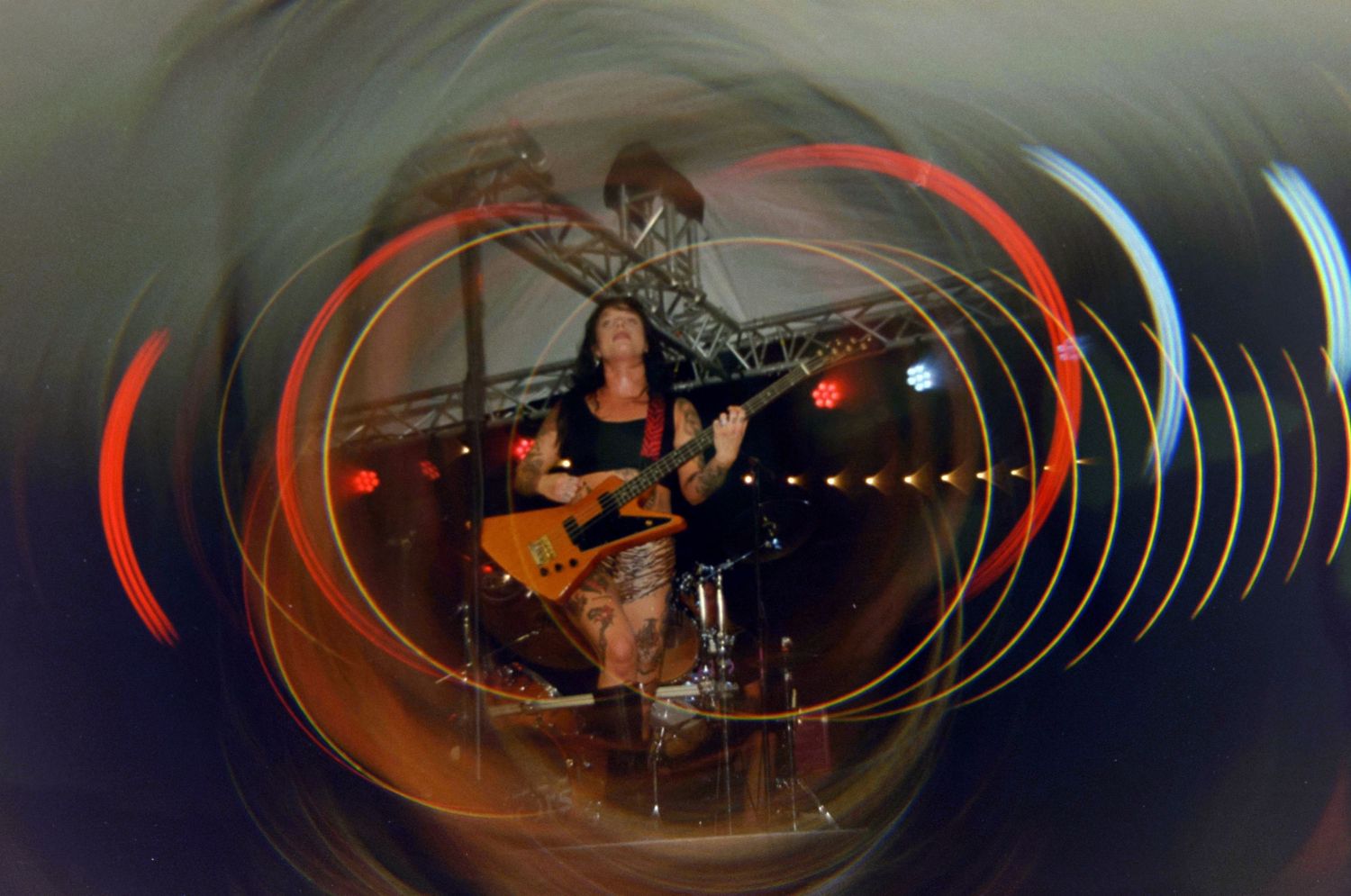 Female guitarist performing on stage with vibrant swirling light effects creating a tunnel visual during a live concert.