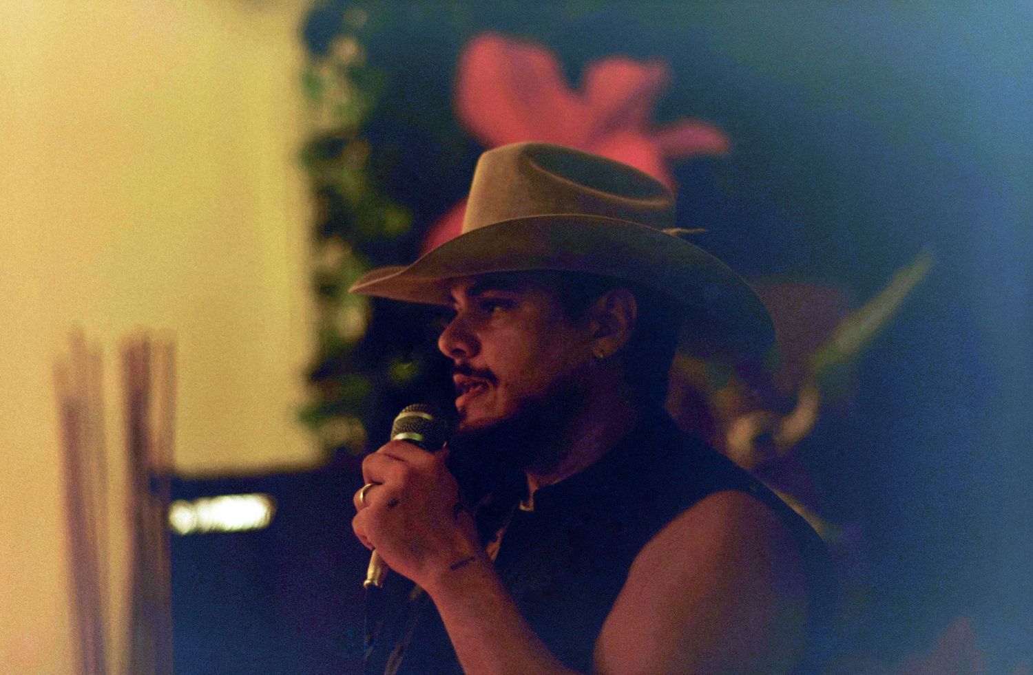 Man in cowboy hat singing into microphone on stage with floral backdrop.